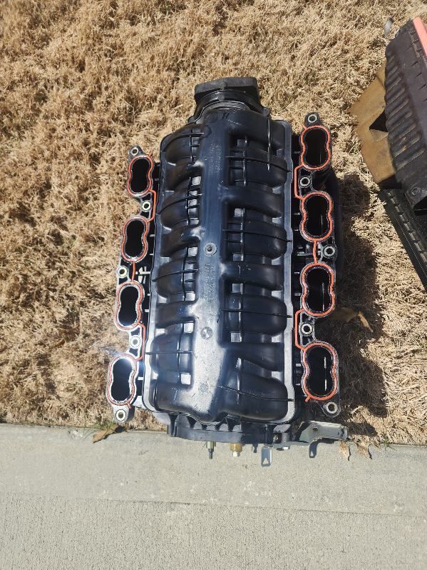 A black engine intake manifold is sitting on the ground