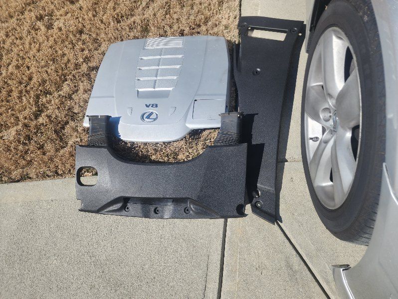 A nissan engine cover is sitting on the sidewalk next to a car