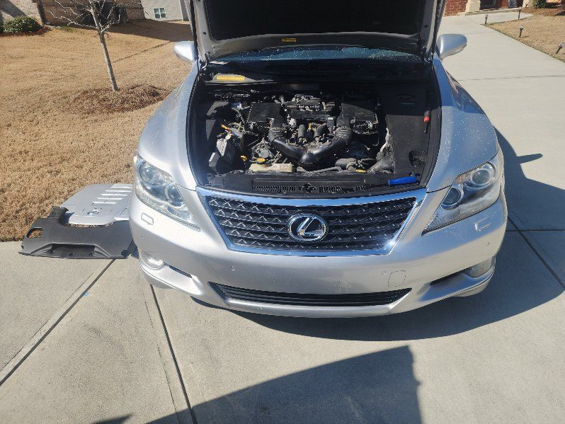 A silver lexus with the hood up is parked on a sidewalk