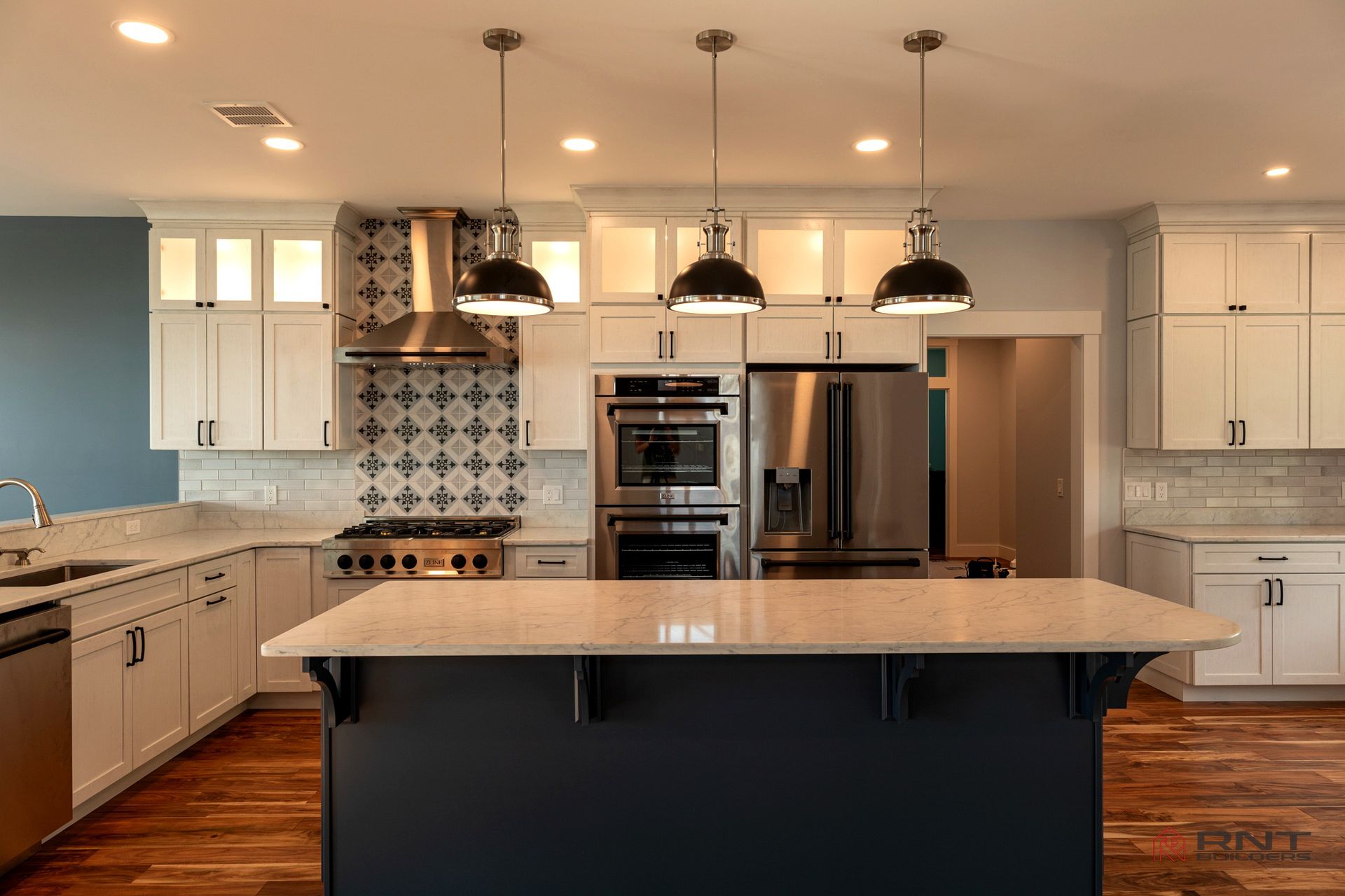 Modern kitchen with white cabinets, a blue island, stainless steel appliances, and pendant lights.
