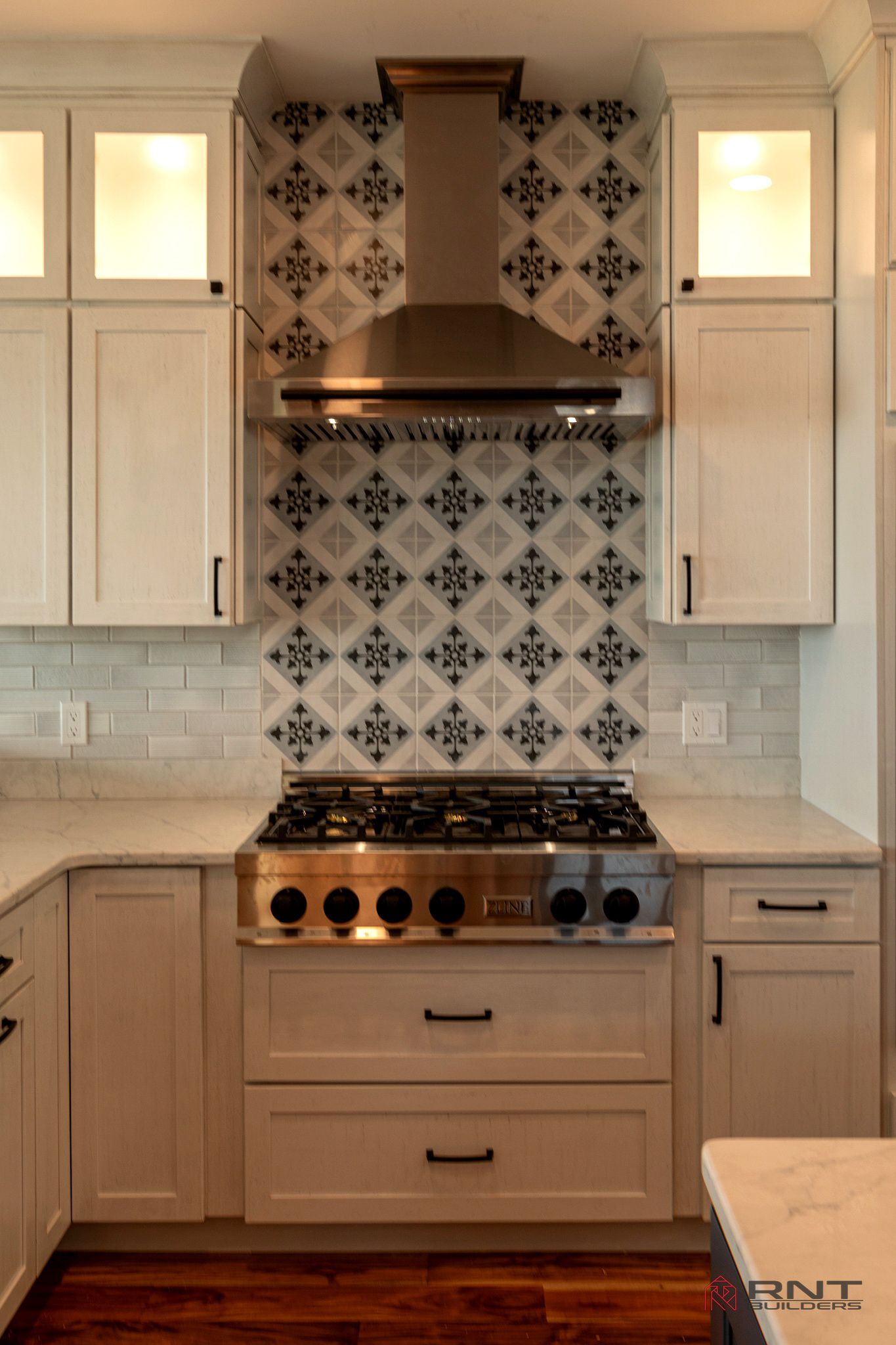 Kitchen with white cabinets, stainless steel appliances, and patterned tile backsplash. The stovetop is centered with a range hood above.