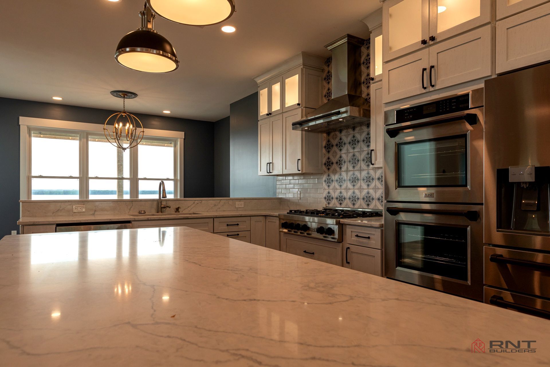 A luxury kitchen with custom white cabinets , stainless steel appliances , and large quartz island.