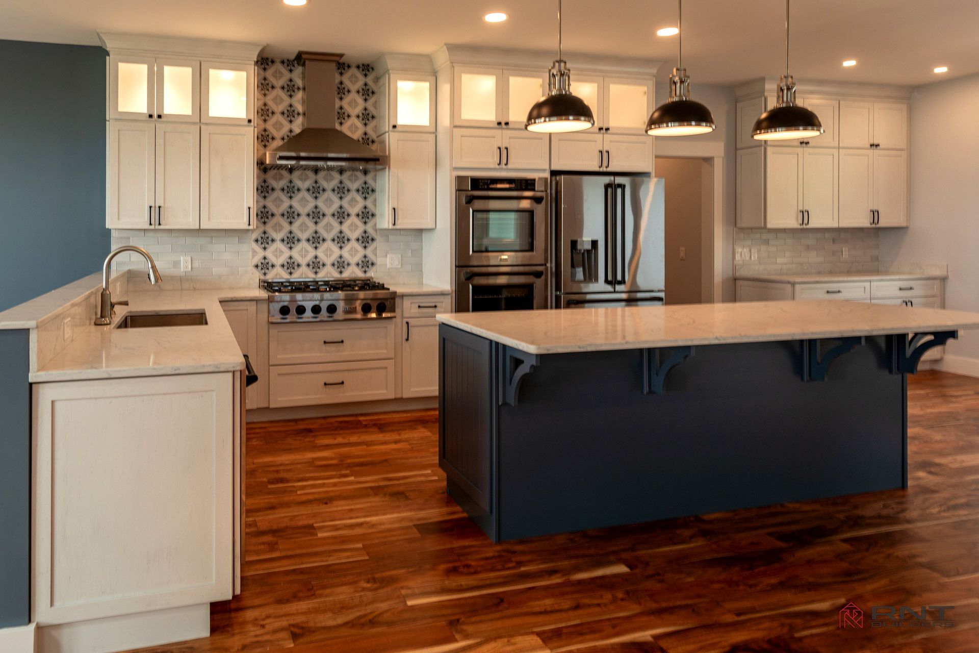 A spacious kitchen with white cabinets, navy island, stainless steel appliances, and hardwood floors. Includes a patterned tile backsplash.