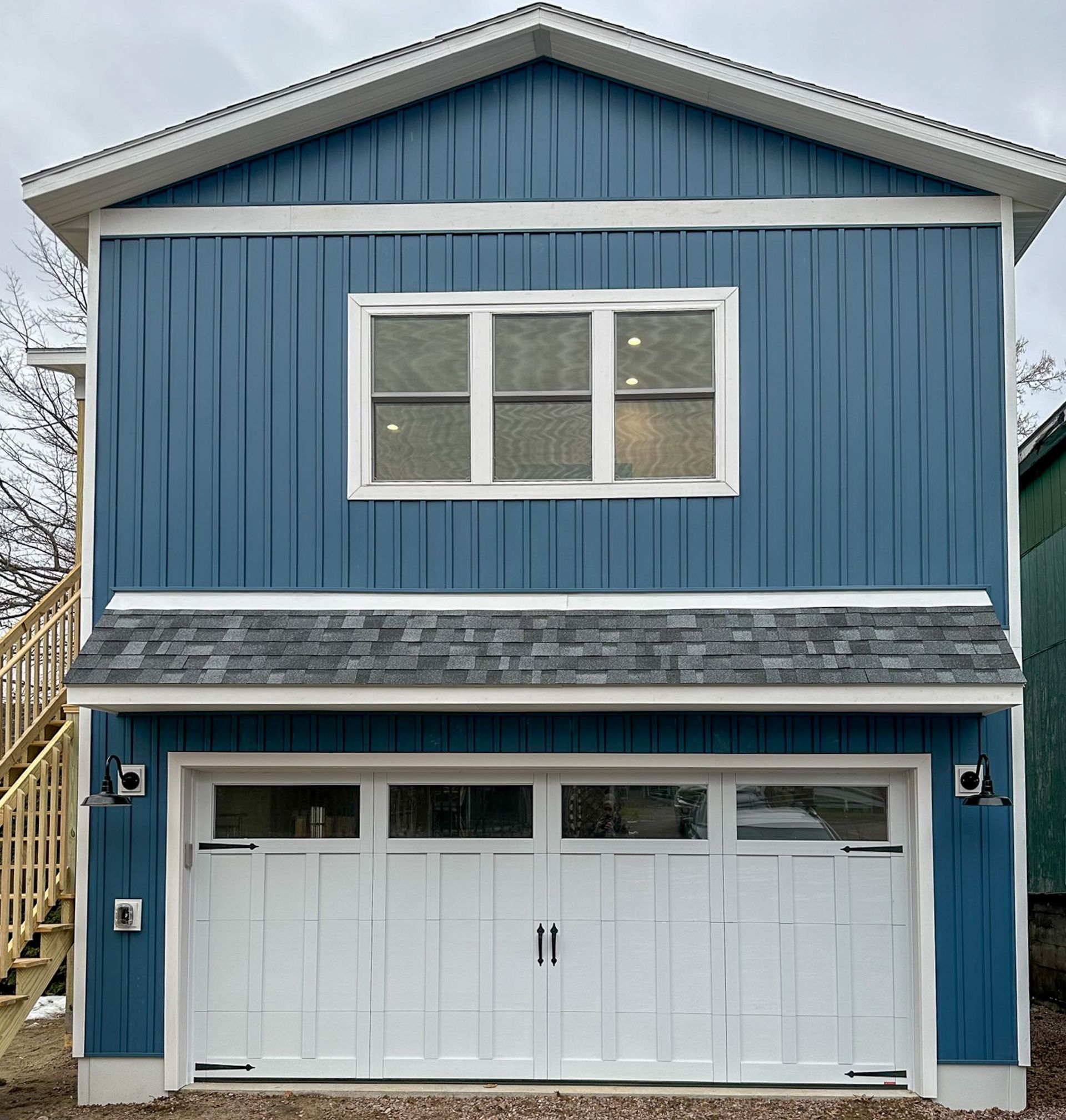 Two-story blue building with white garage door below a triple window; wooden stairs on the left.
