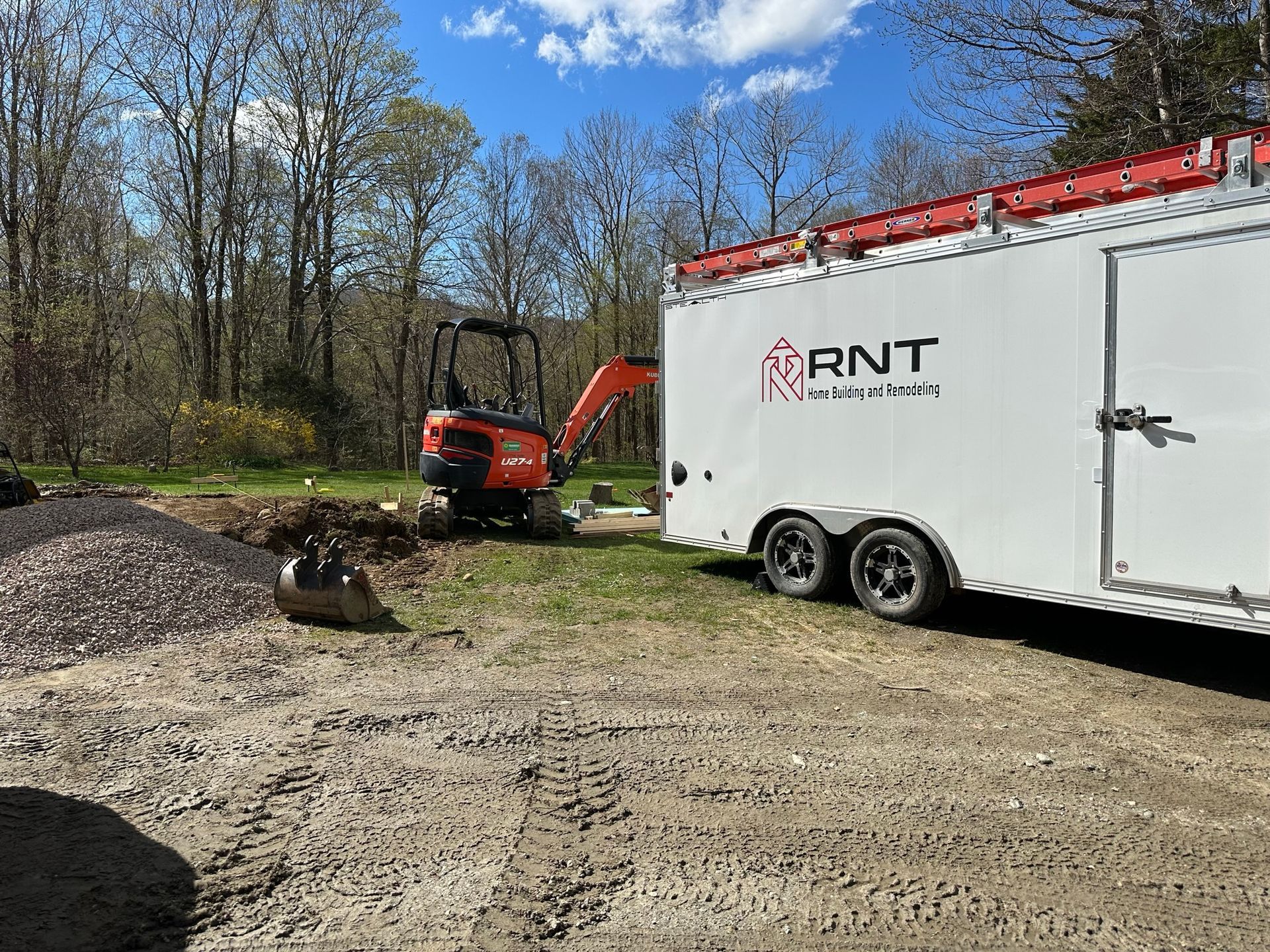 Mini excavator digging beside a white trailer labeled 