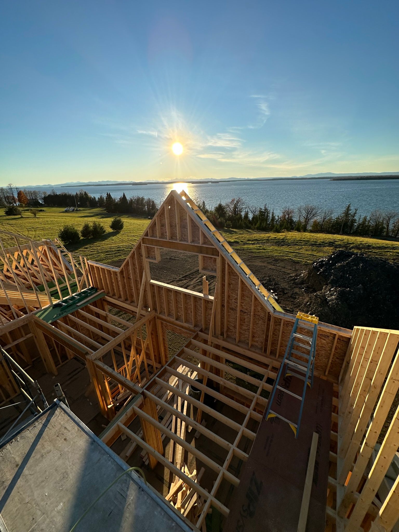 Wooden house frame under construction, with a water view and bright sun.