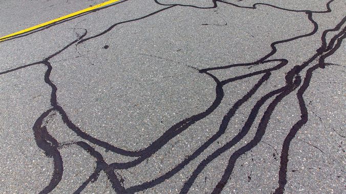 A close up of a cracked asphalt road with a yellow line.