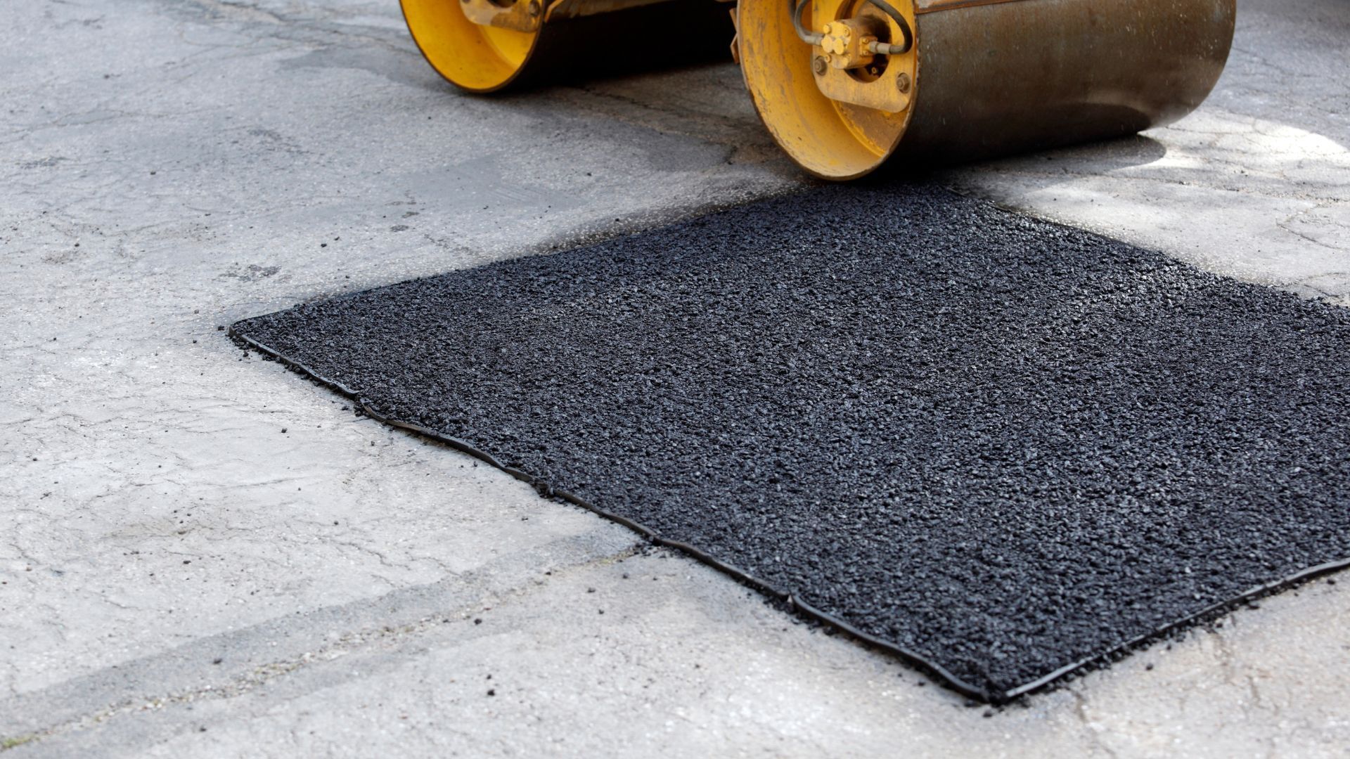 A yellow roller is rolling a piece of asphalt on the ground.