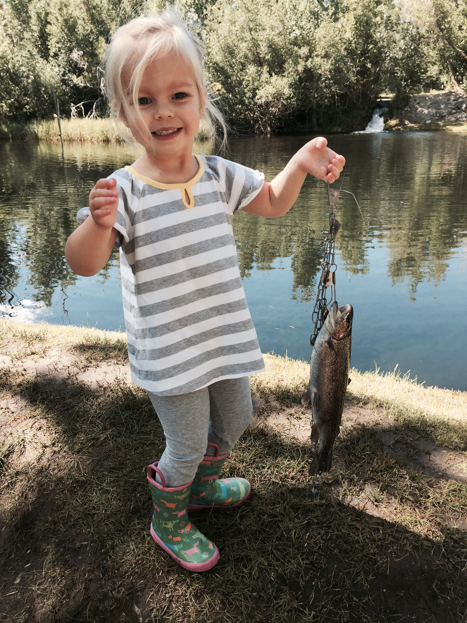 A little girl is holding a fish in front of a lake.