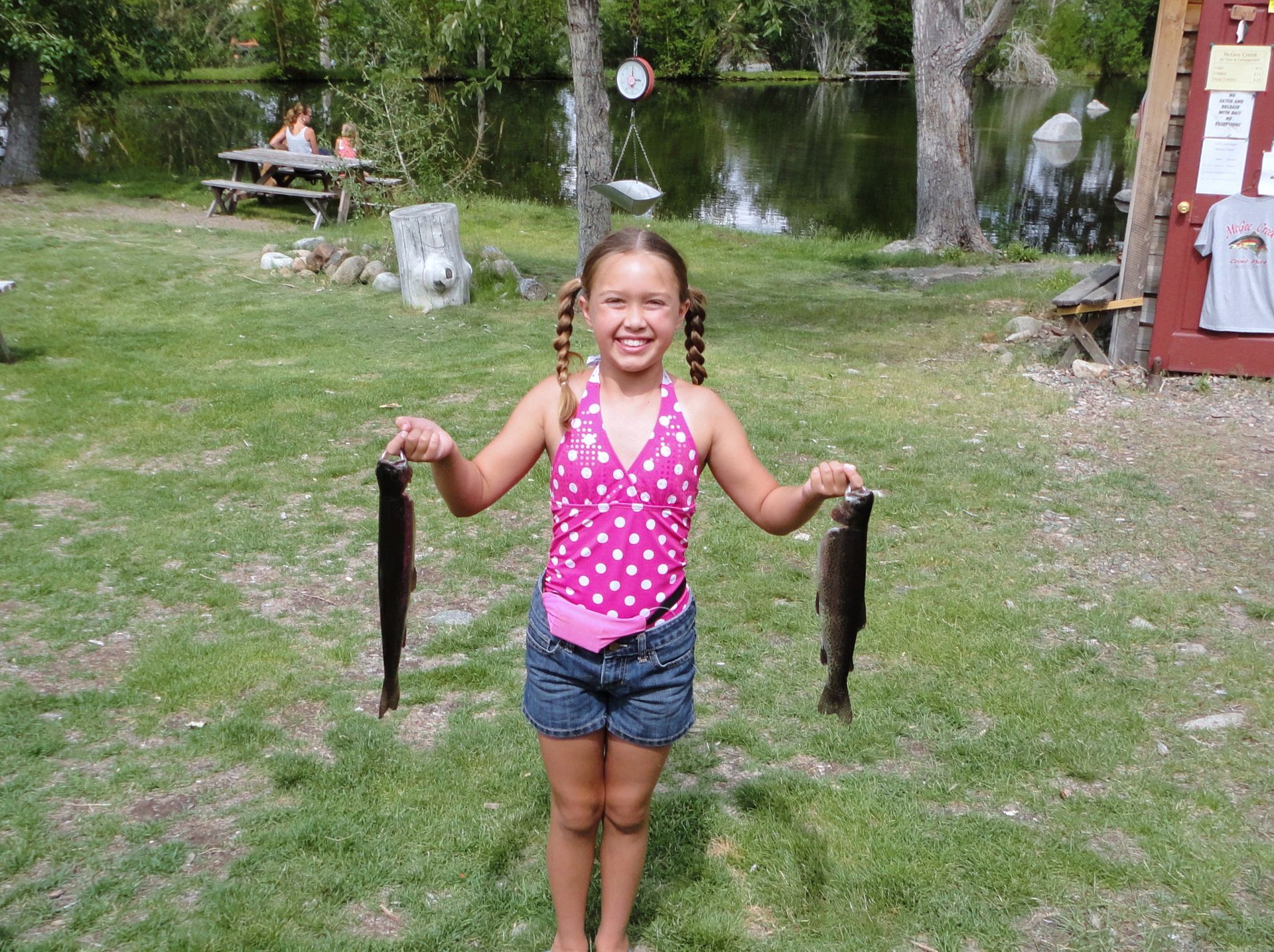 A little girl in a pink polka dot tank top is holding two fish in her hands.