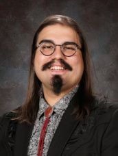 A man with long hair and a beard is wearing glasses and a plaid shirt.