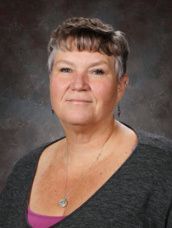 A woman in a horseshoe print shirt is smiling for a picture.