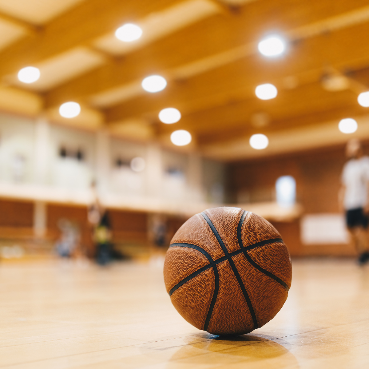 A basketball is sitting on a wooden floor in a gym