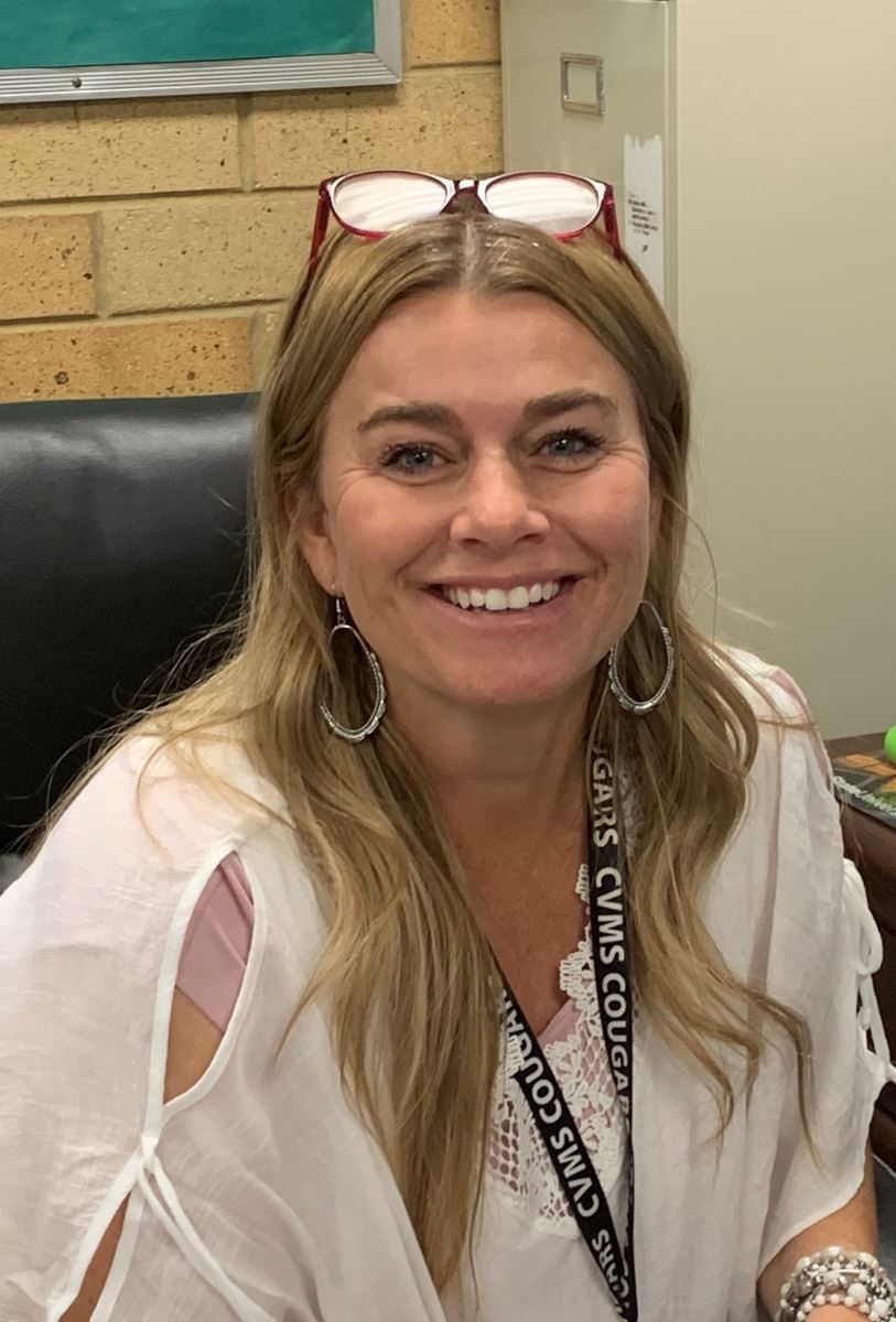 A woman wearing glasses and a lanyard is smiling for the camera.