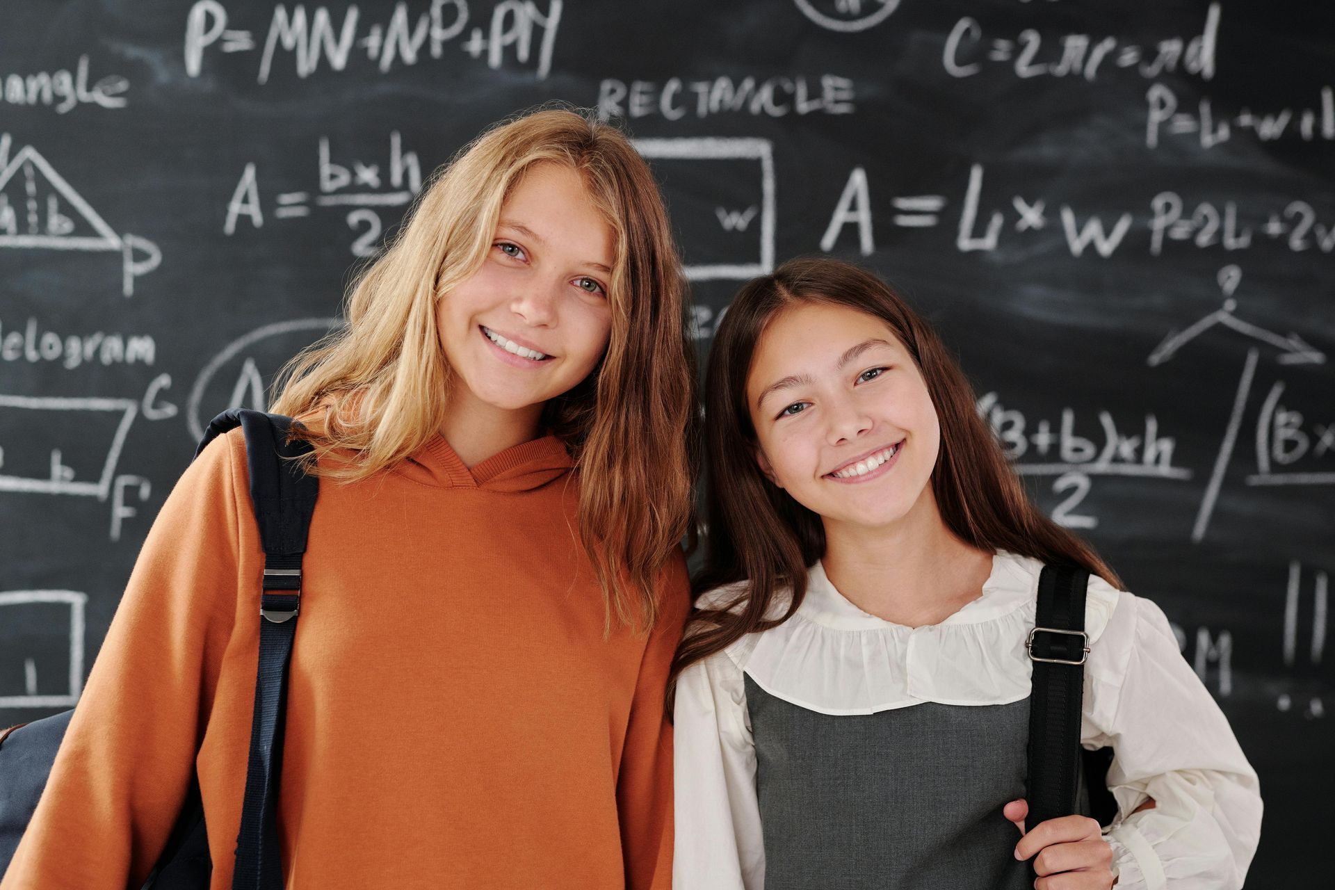 Two girls are standing next to each other in front of a blackboard.