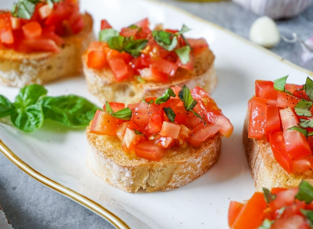 Bruschetta: pane tostato condito con pomodori a cubetti, basilico e condimenti su un piatto bianco.