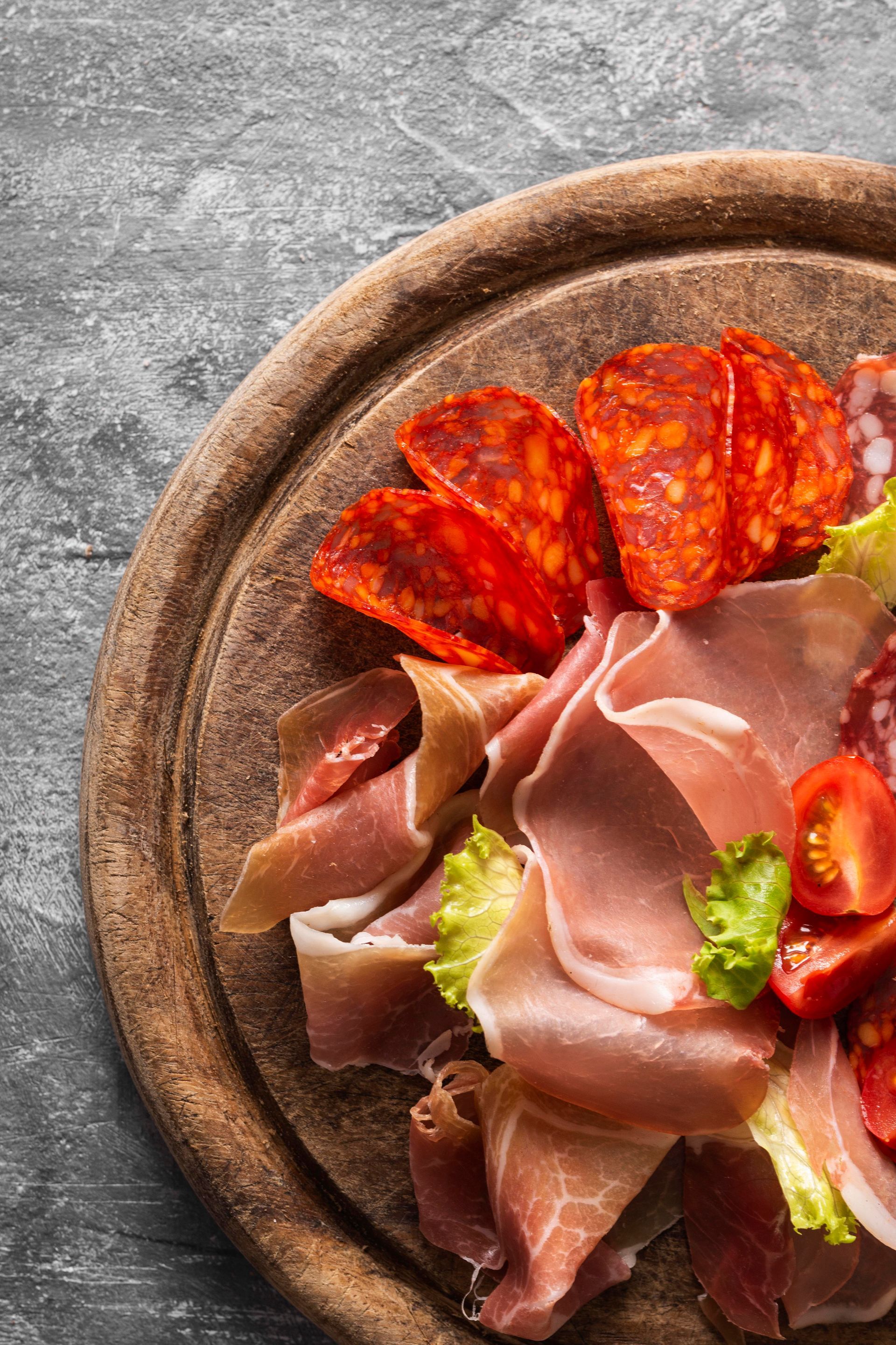 Tagliere di salumi con salame, chorizo, prosciutto, pomodori e lattuga.