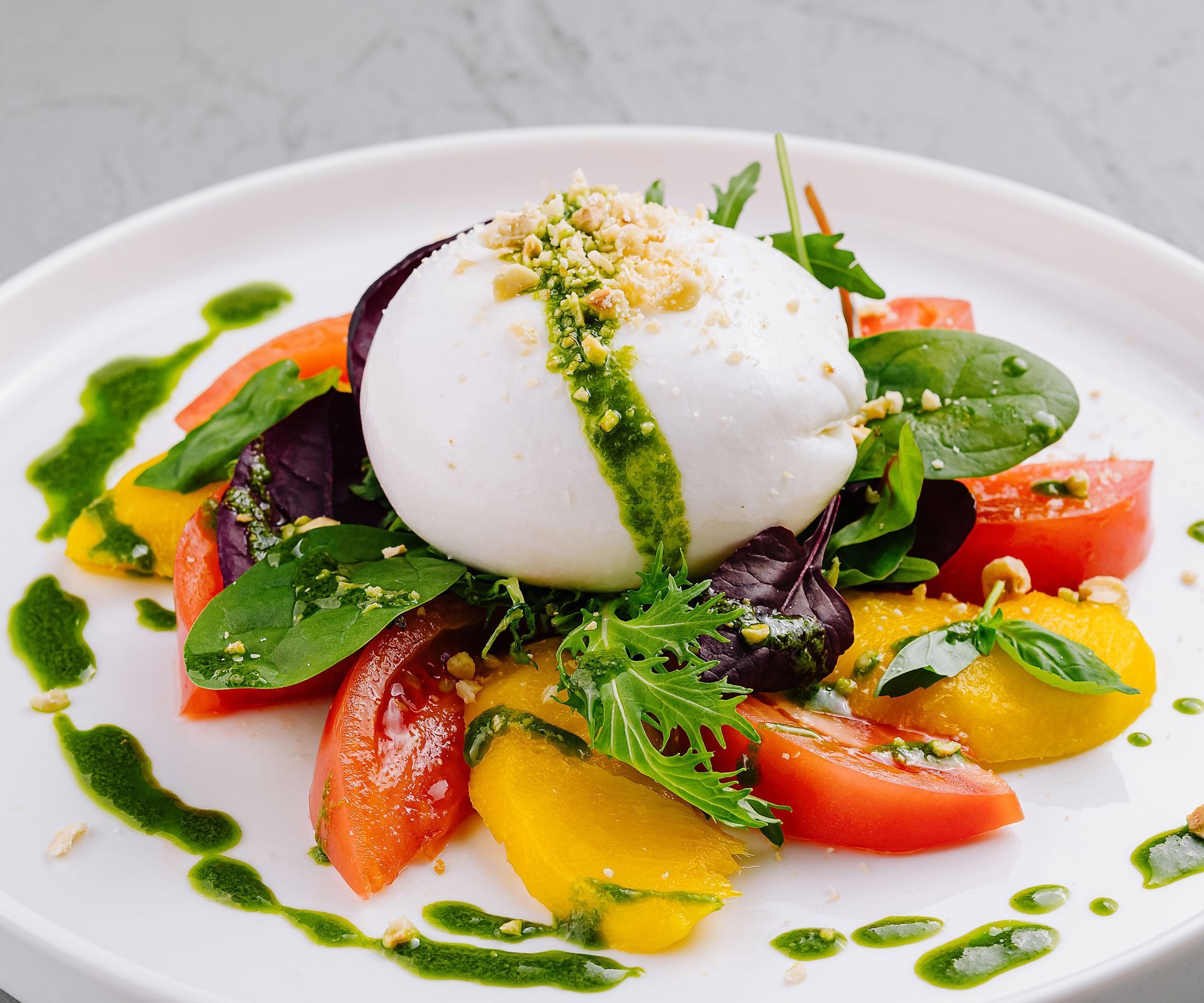 Insalata di burrata con pomodori antichi, basilico e pesto su un piatto bianco.