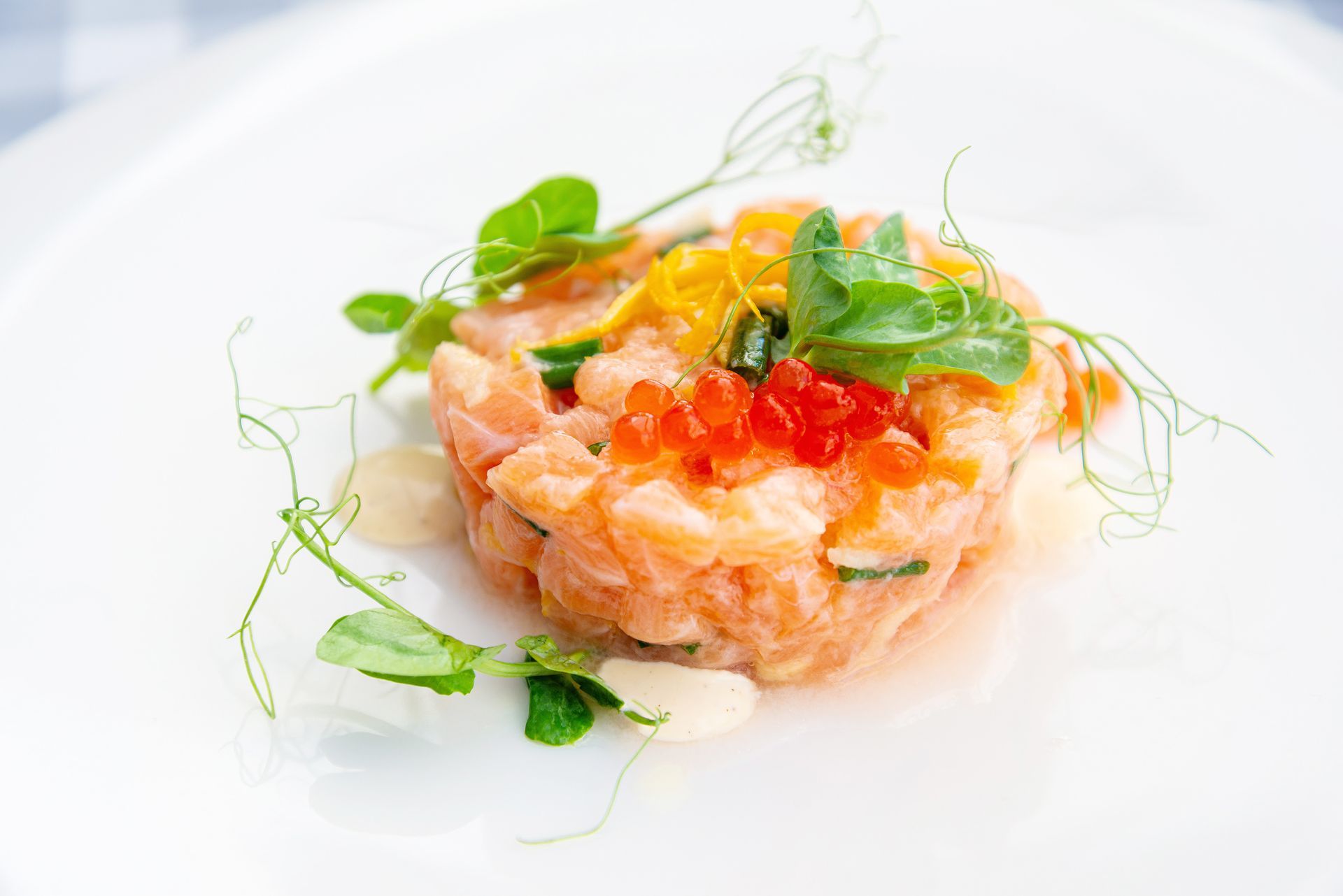 Tartare di salmone su un piatto bianco, guarnita con uova di pesce e microgreens.