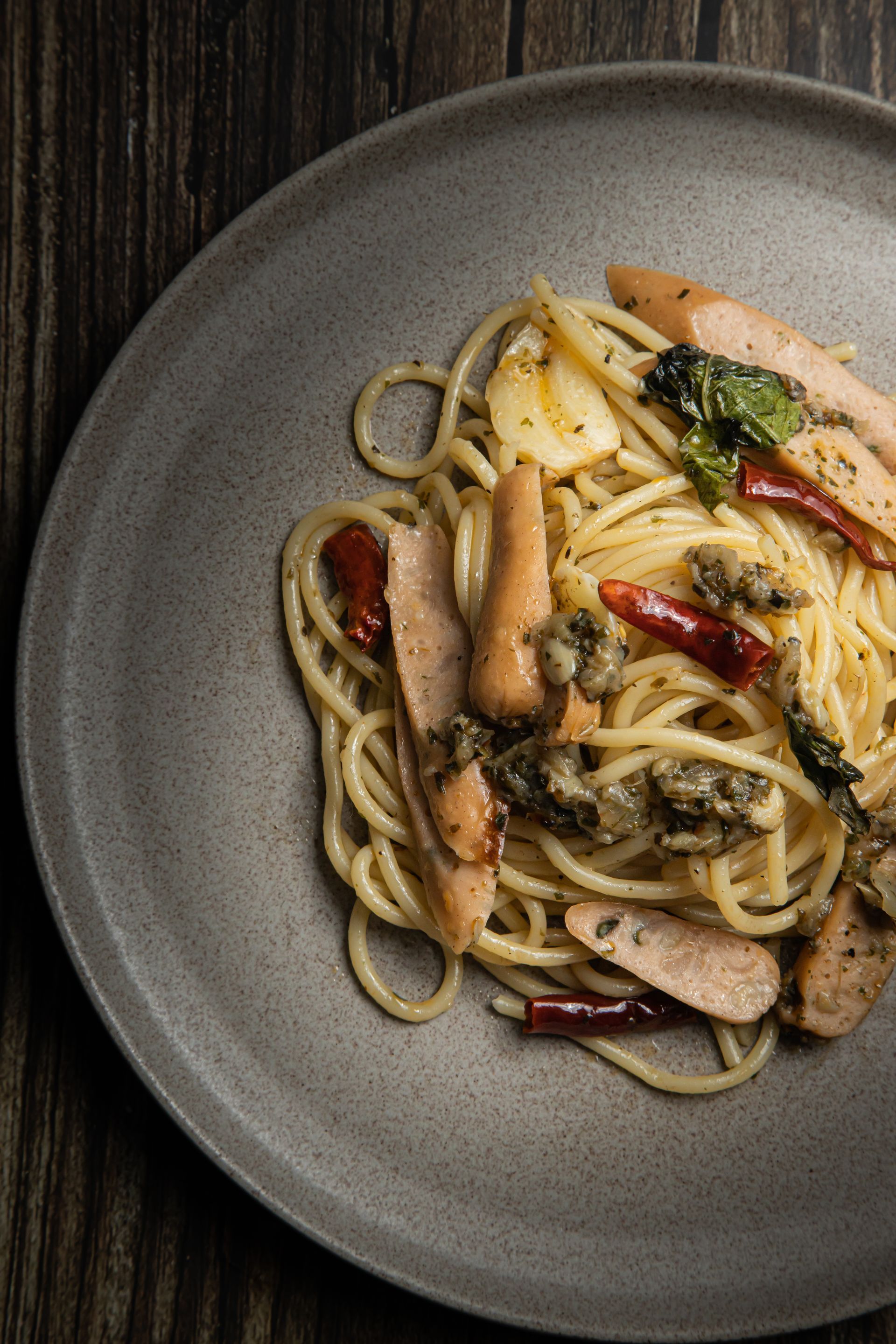 Piatto di spaghetti con salsiccia, erbe aromatiche e peperoni rossi su un piatto grigio.