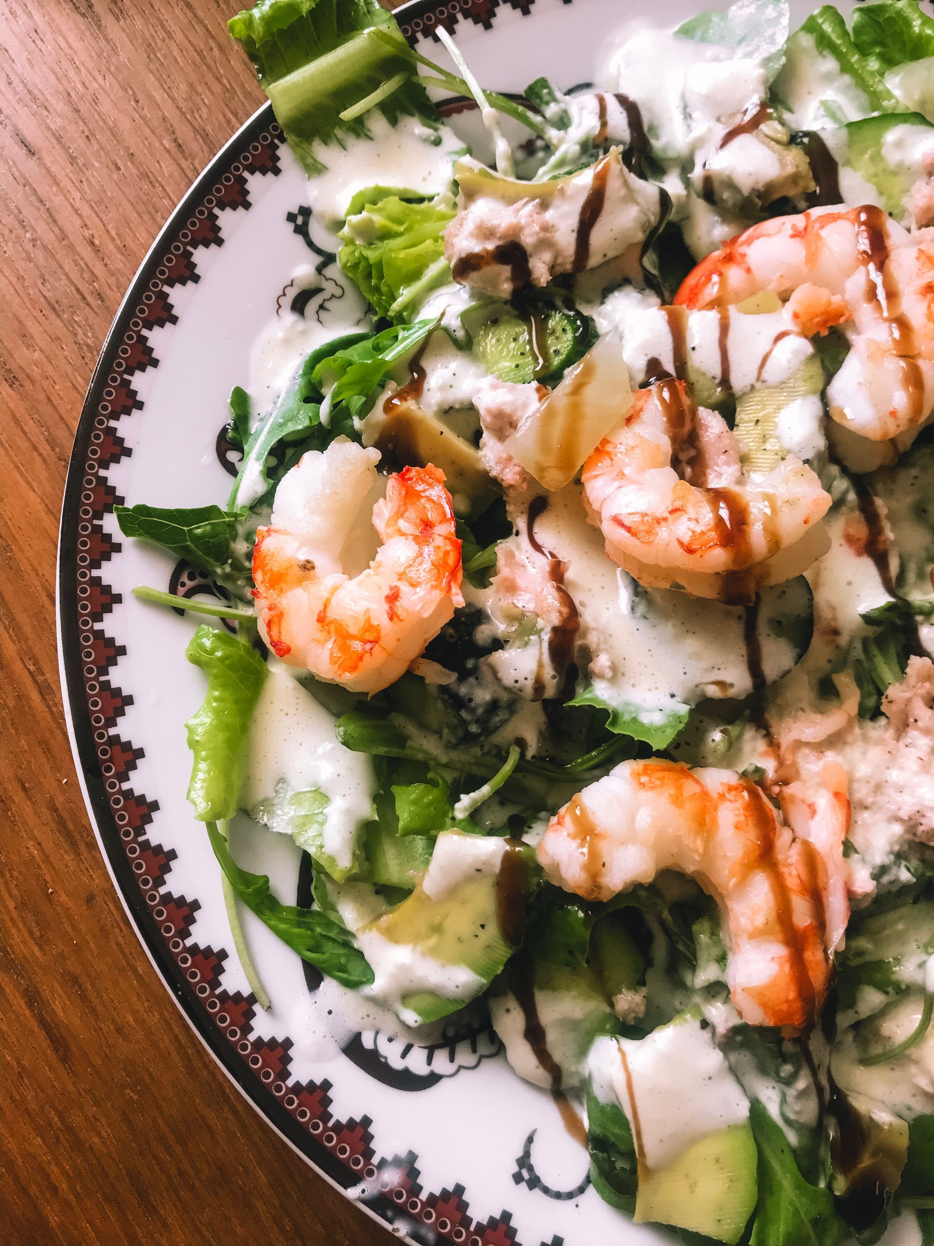 Insalata di gamberi con condimento cremoso, avocado e carciofi su un piatto decorativo, condita con glassa balsamica.