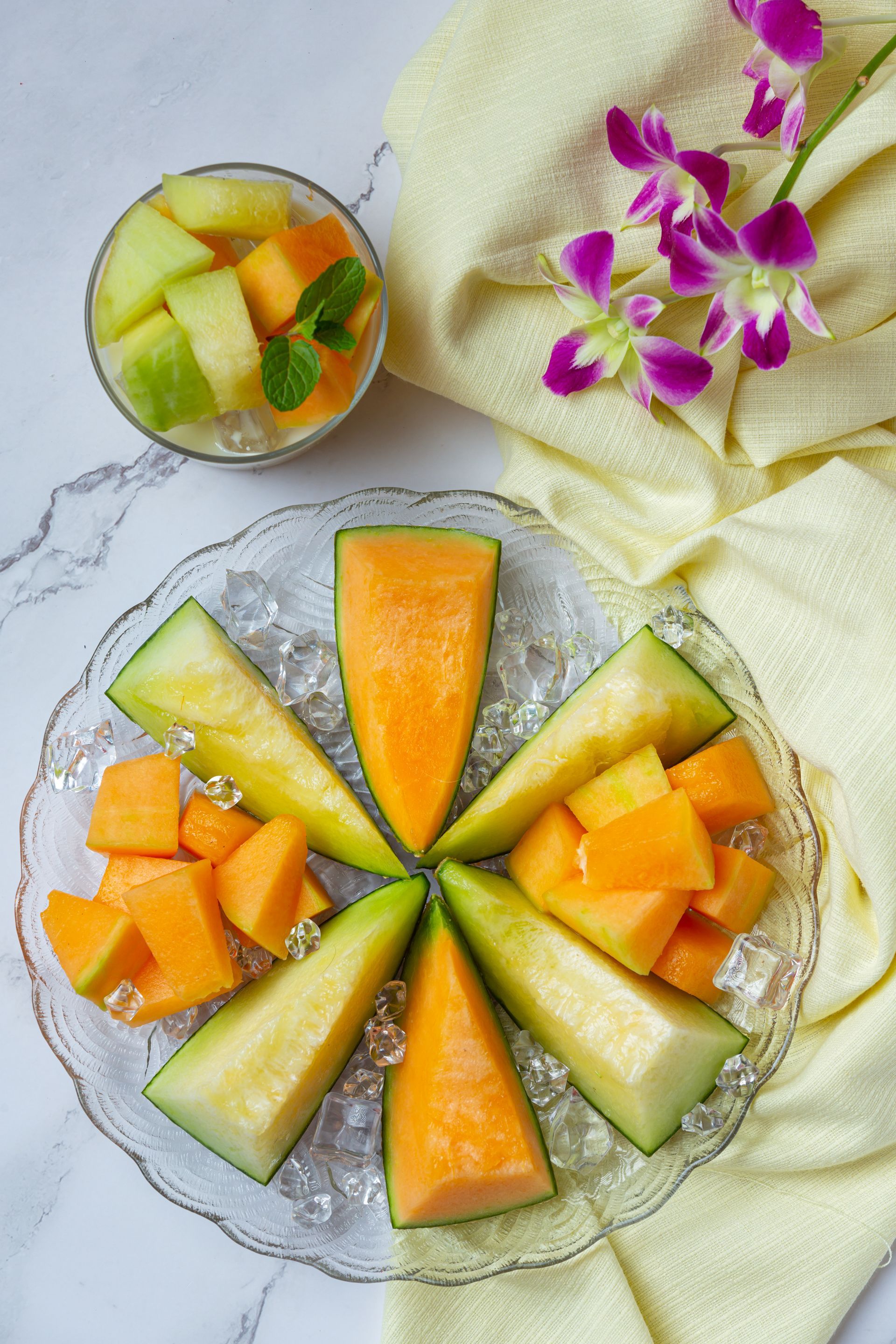 Fette e cubetti di melone disposti su un piatto trasparente, guarnito con menta. 