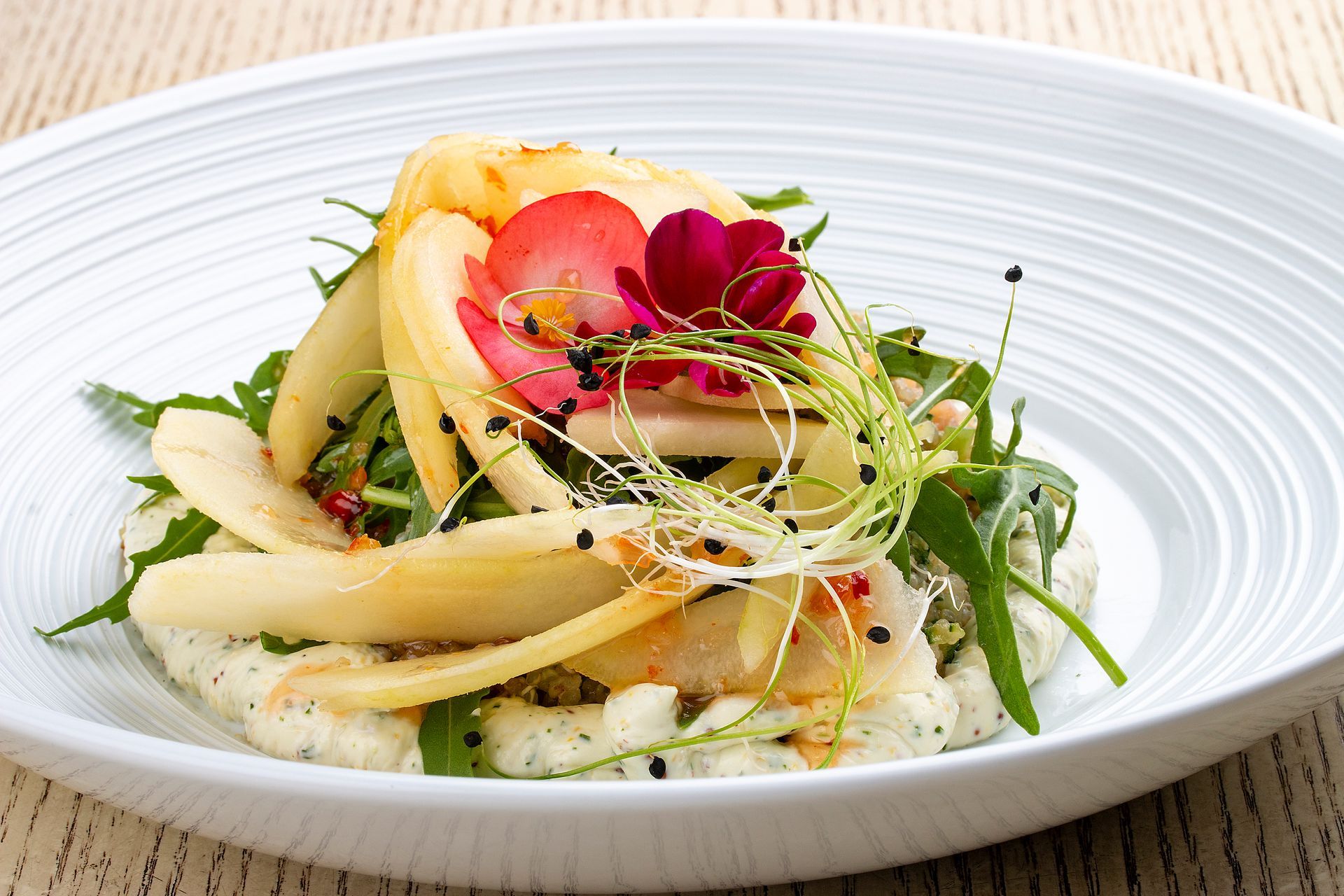 Elegante insalata di pere con rucola, microgreens e fiori commestibili su un piatto bianco.