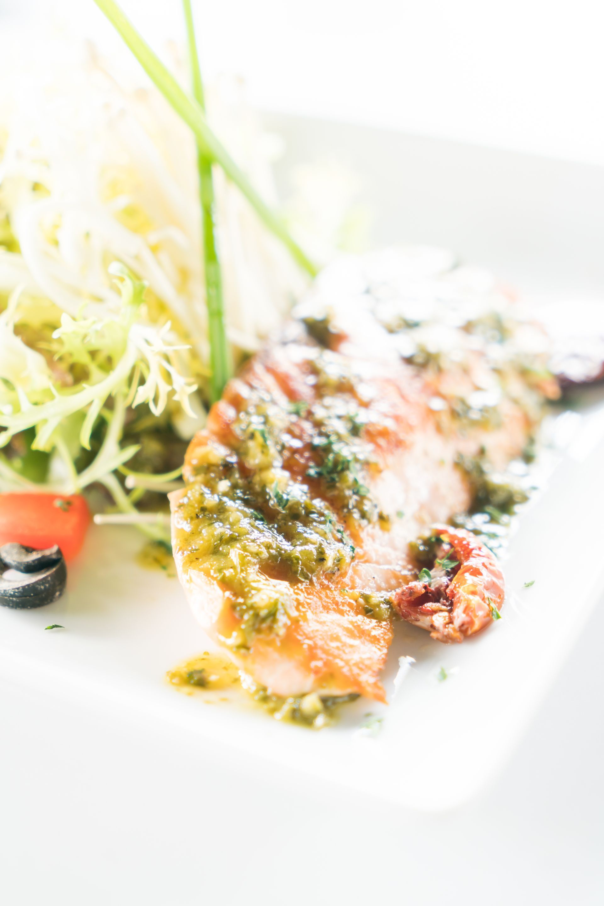 Pesce alla griglia con pesto e insalata su un piatto bianco.