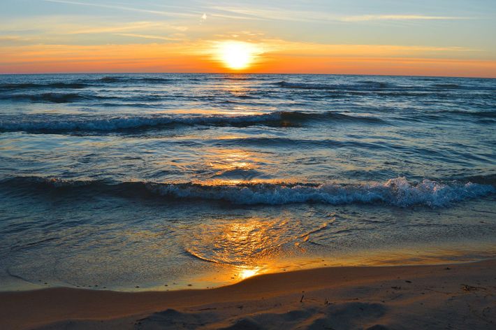 The sun is setting over the ocean and the waves are crashing on the beach.