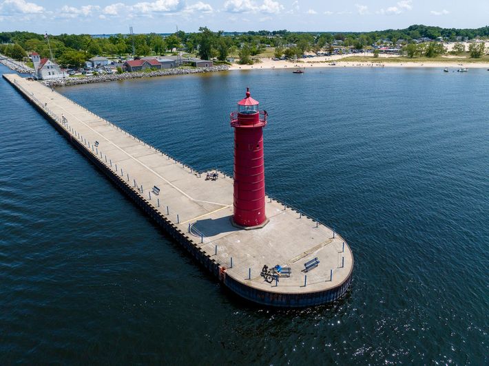 An aerial view of a red lighthouse on a pier in the middle of a body of water.