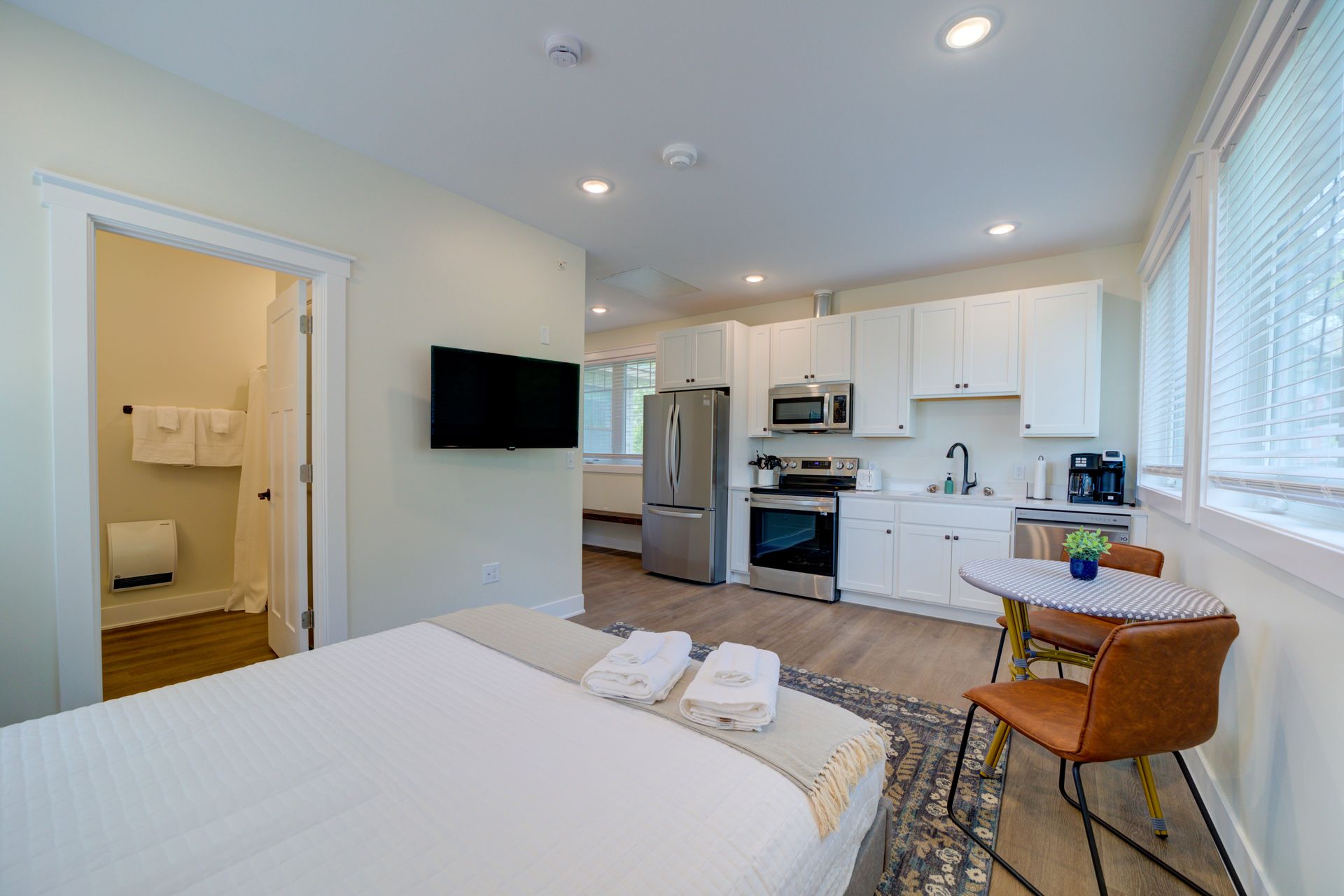 A bedroom with a bed , table , chairs and a kitchen.
