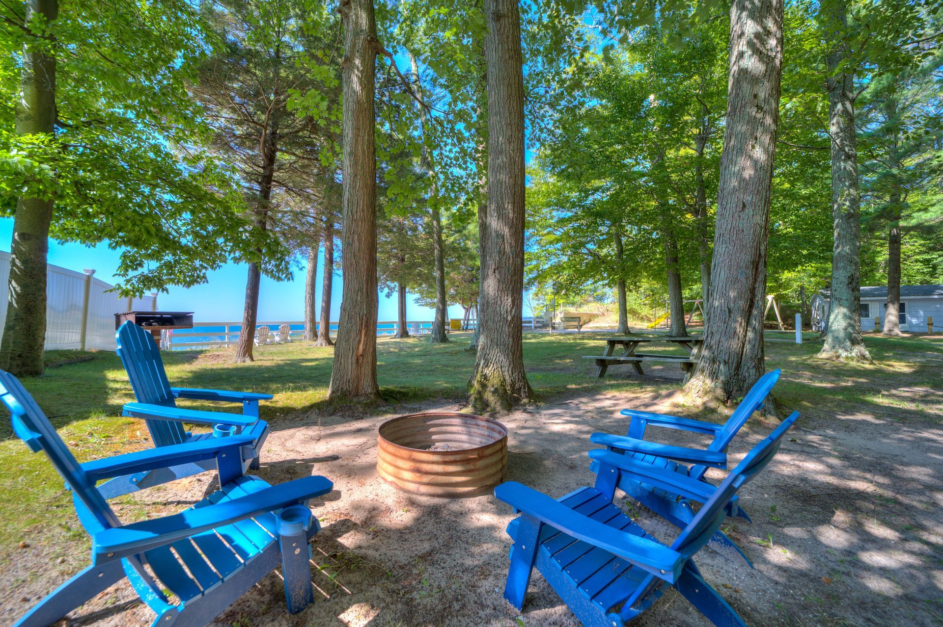A group of blue chairs are sitting around a fire pit in the woods.