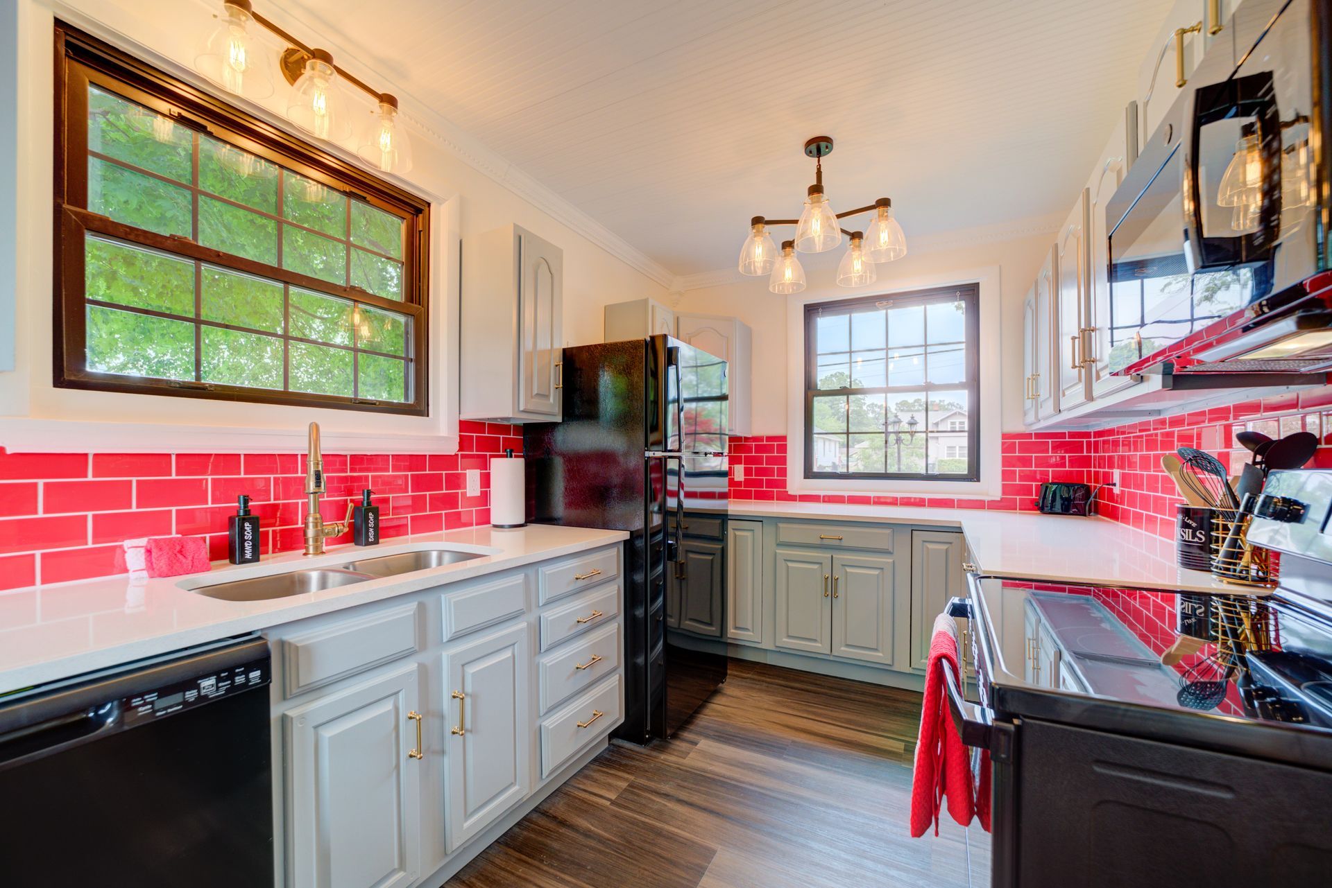 A kitchen with red brick tiles , white cabinets , black appliances , and a sink.
