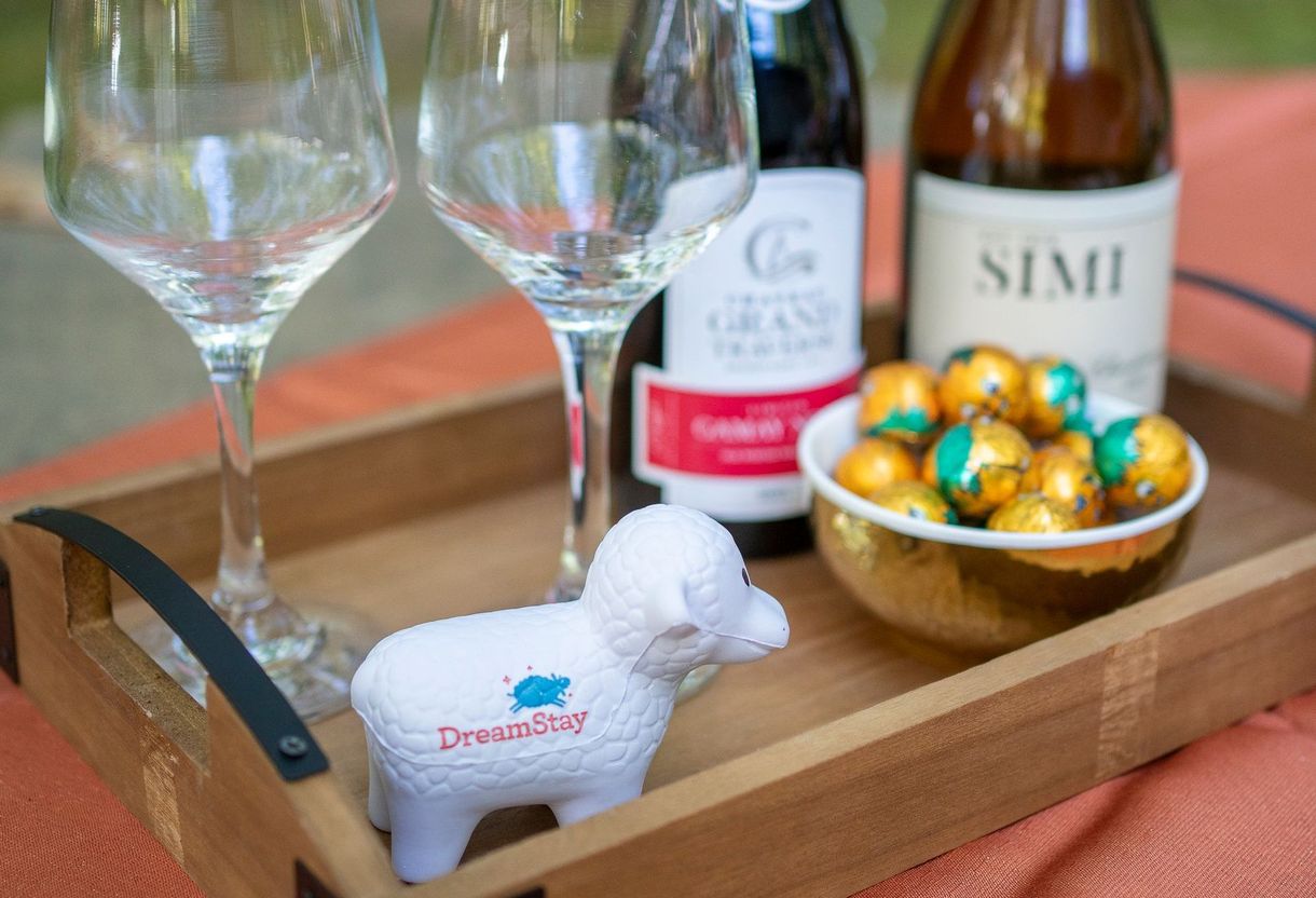 A wooden tray with two wine glasses , a bottle of wine and a bowl of chocolate eggs.