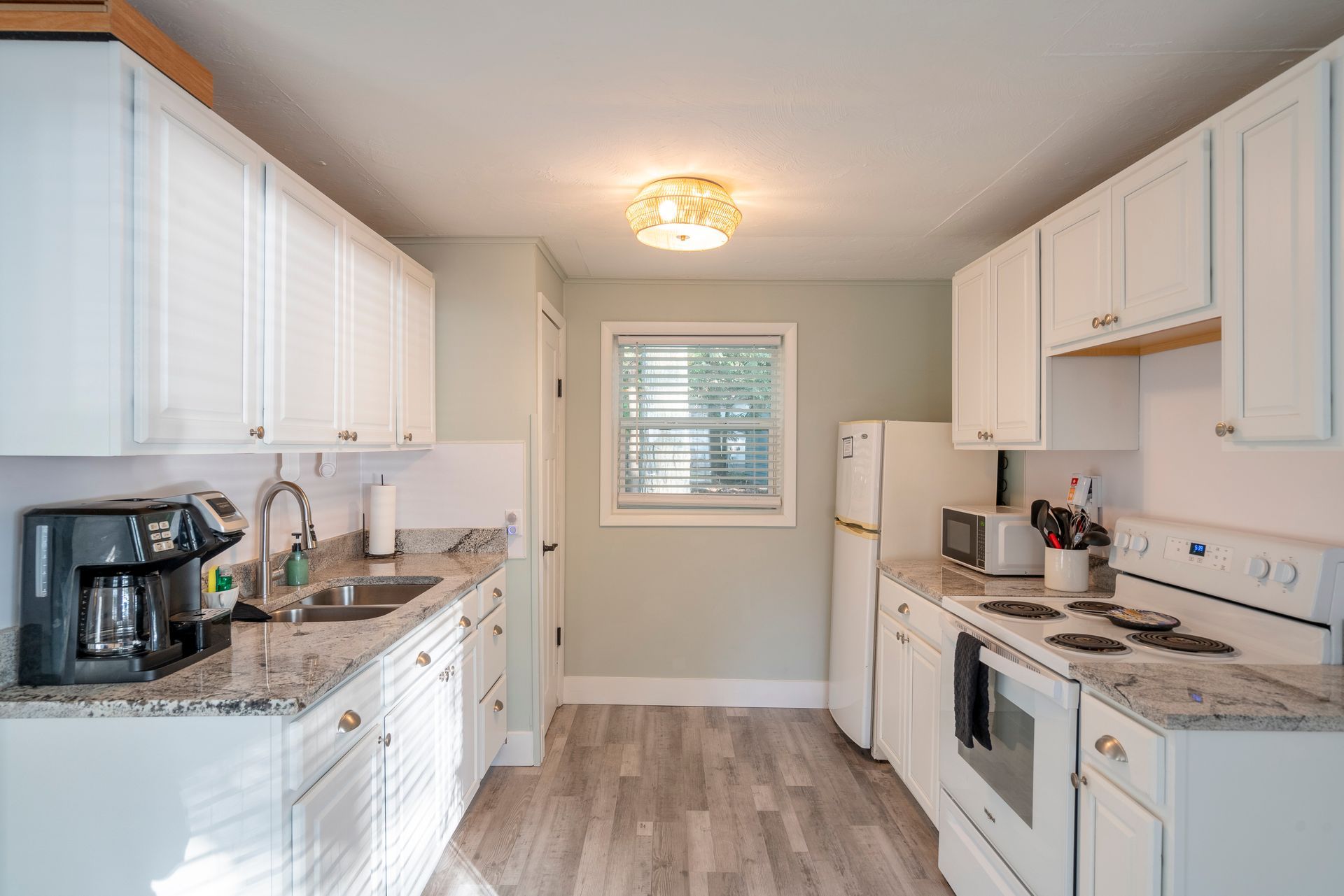 A kitchen with white cabinets , a stove , a refrigerator , a sink , and a window.