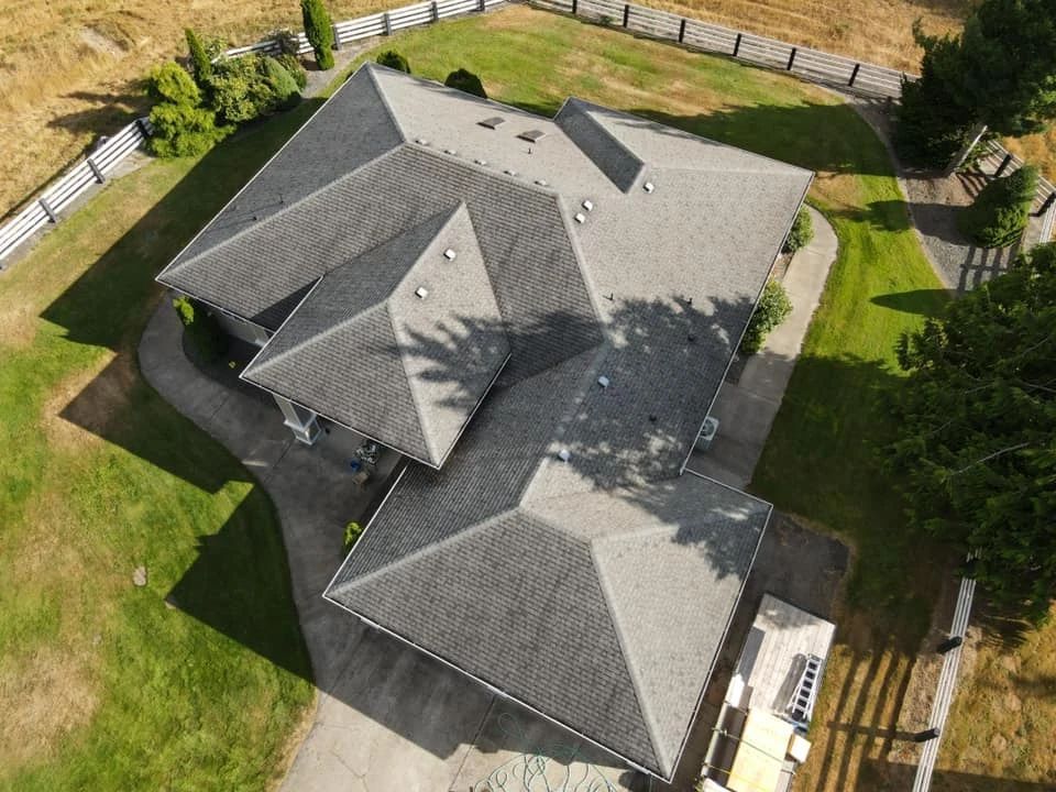 An aerial view of a house with three roofs and a driveway.