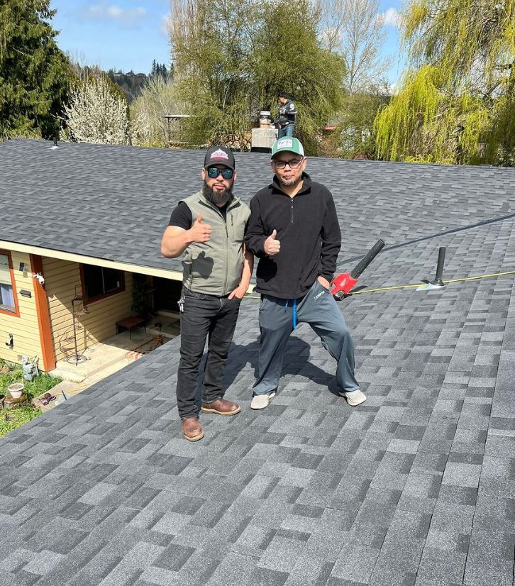 Two men are standing on top of a roof giving a thumbs up.