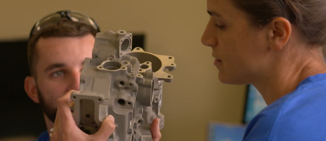 A man and a woman are looking at a piece of metal.