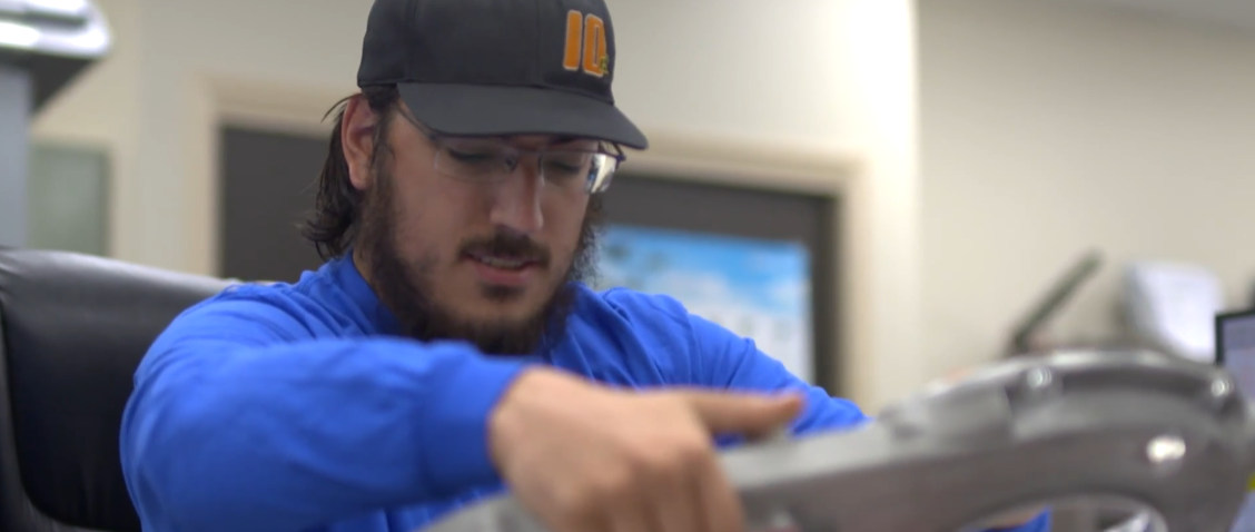 A man wearing a hat and glasses is working on a piece of metal.