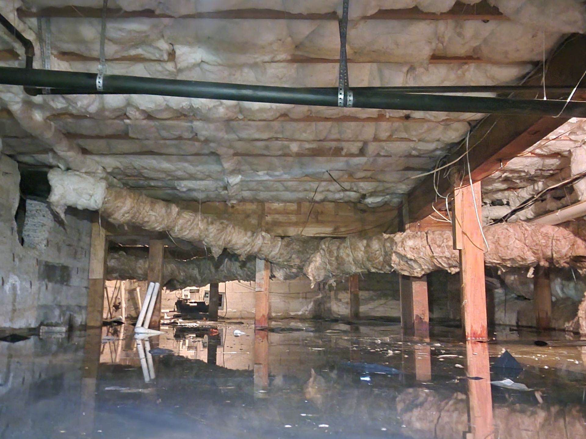 Flooded crawlspace with damaged insulation and vapor barrier, highlighting the need for drainage.