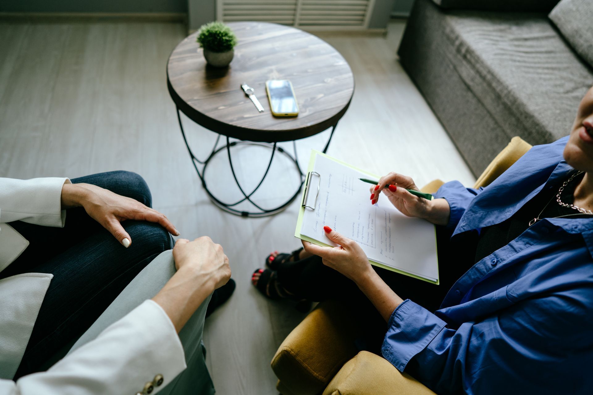 A counselor holding a clipboard and pen while talking to a client seated in a modern office setting