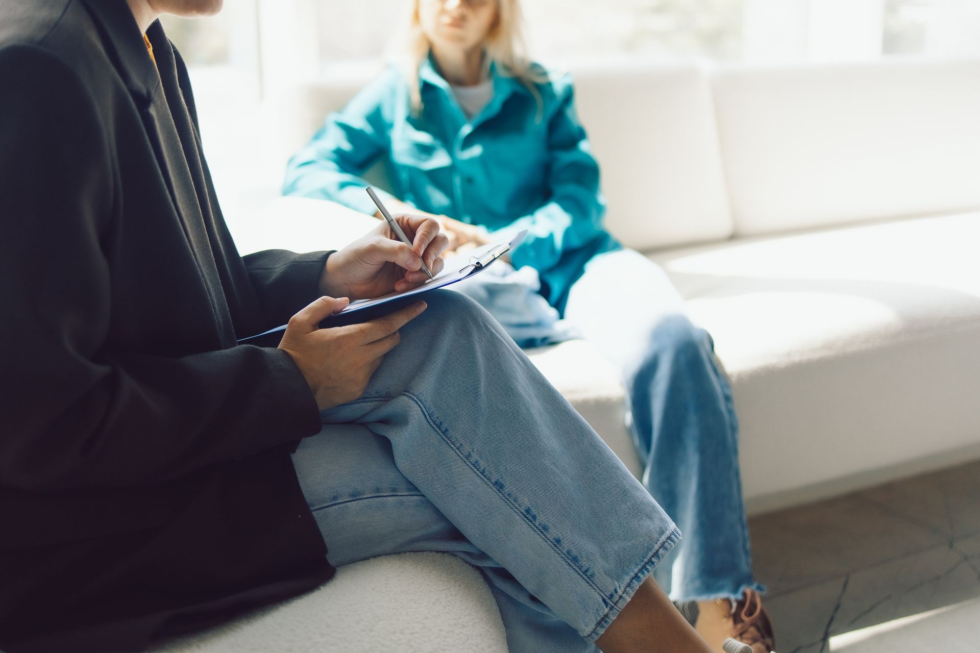 A therapist writing notes on a clipboard during a counseling session with a client on a sofa
