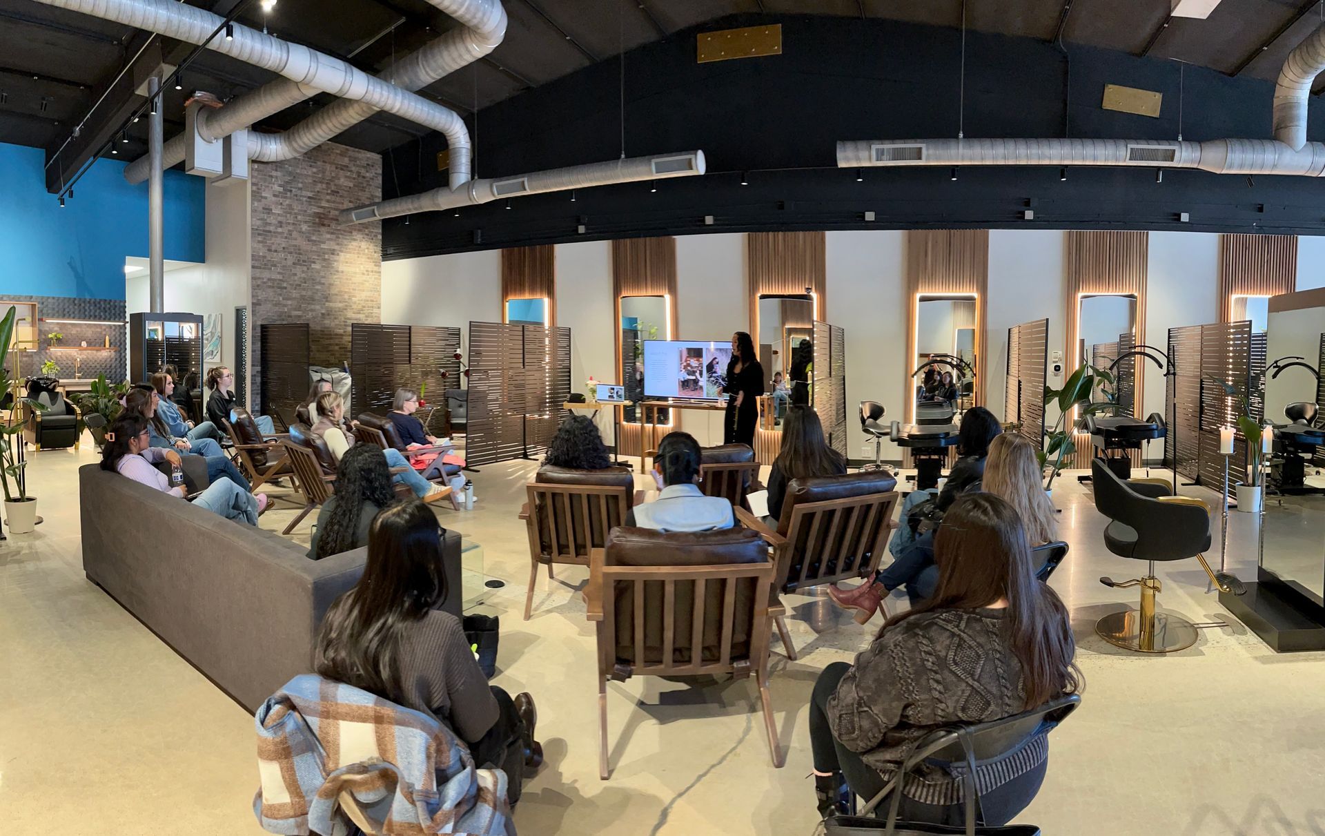Hair salon interior with mirrors, chairs, and plants; wood and black accents.