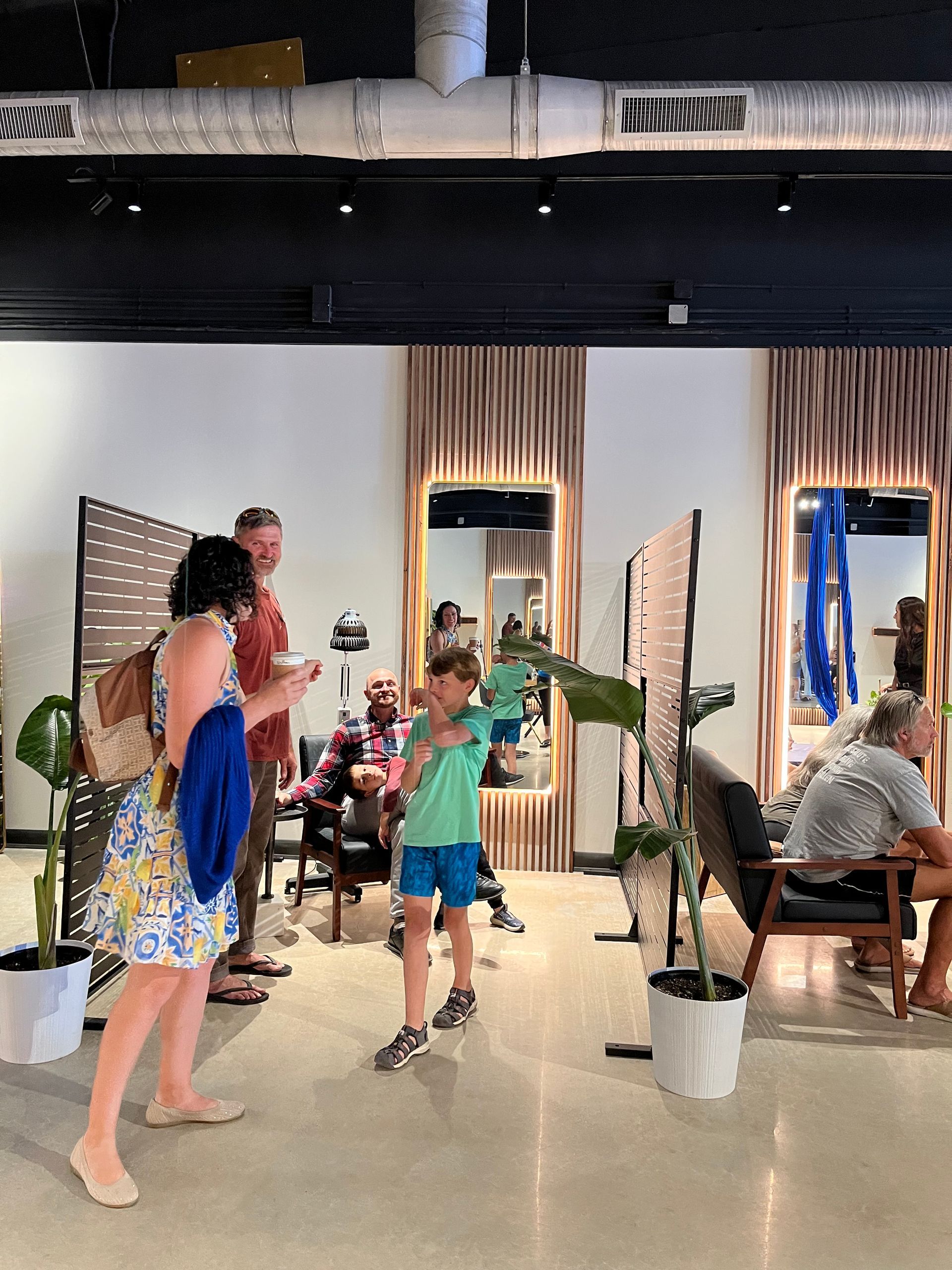 Hair salon interior with mirrors, plants, black ceiling, and styling stations.