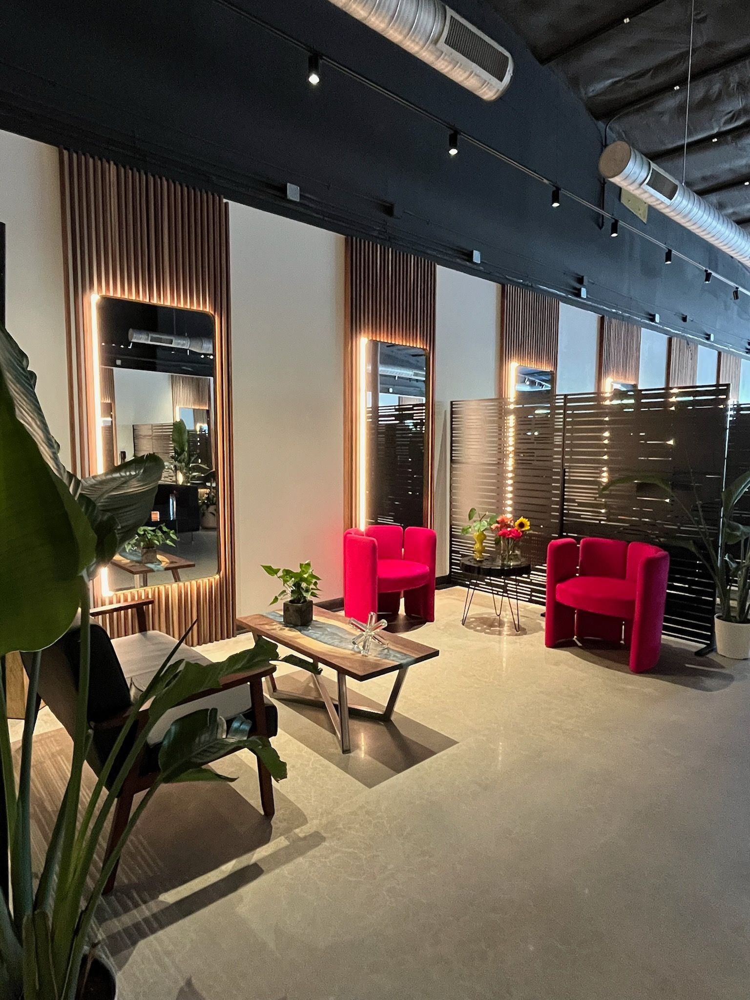 Modern salon interior with pink chairs, mirrors, plants, and a waiting area.