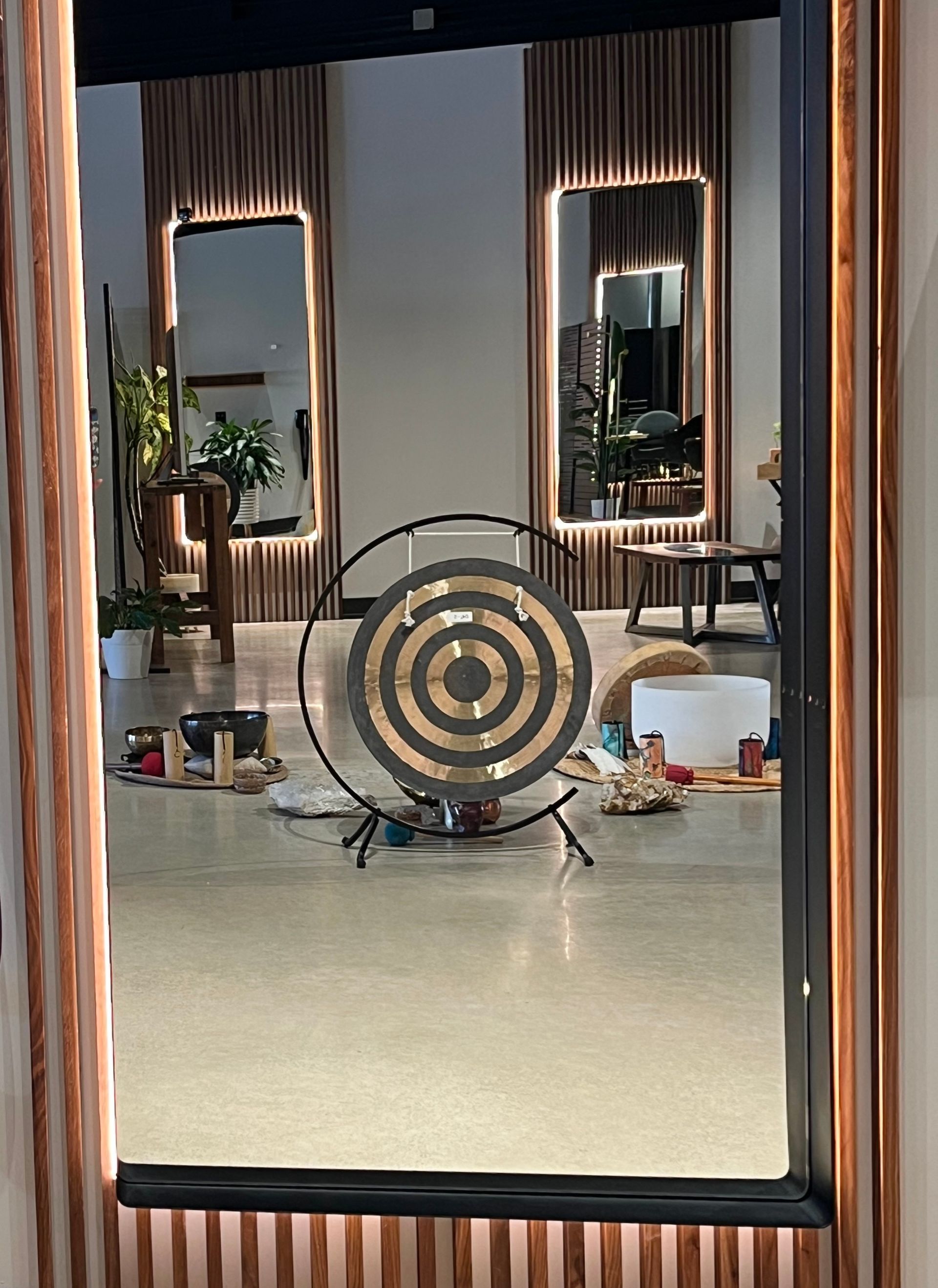 Woman with long, straight red and black hair; looking right near a geometric-lit mirror.