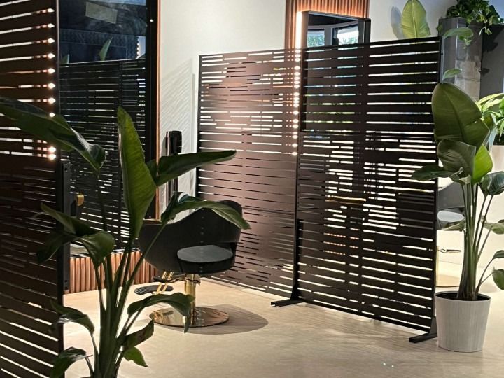Hair salon interior with black slatted dividers, plants, and a stylist chair.