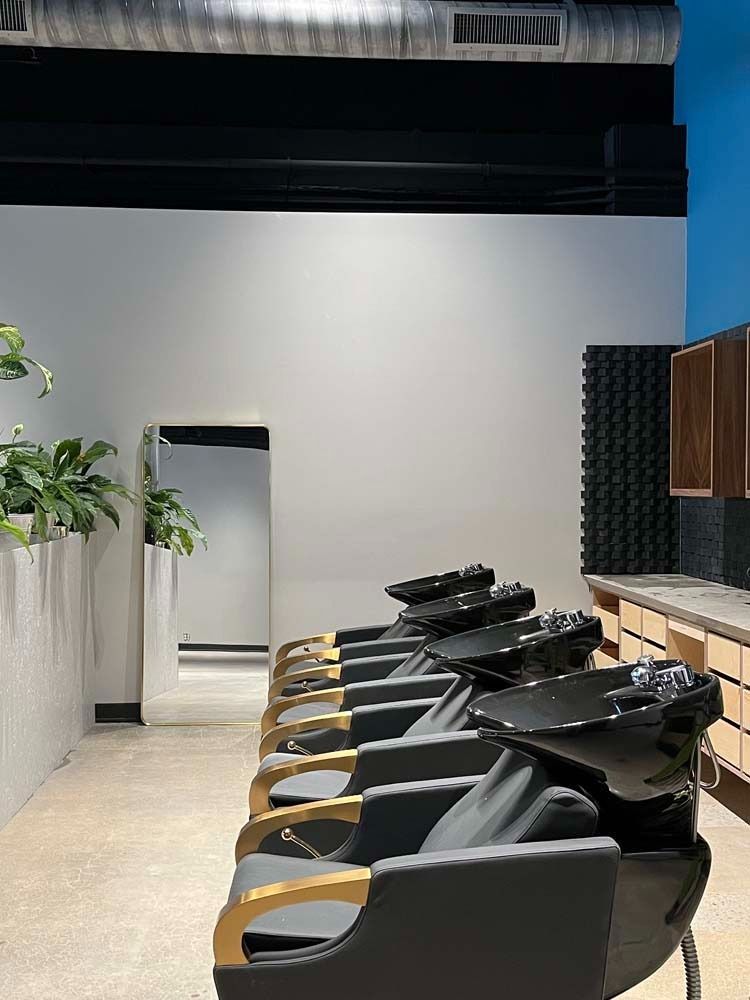 Hair salon interior with wash stations in a row, mirror, and cabinetry. Beige floor, white walls.