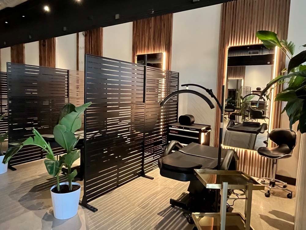 Salon interior: black dividers, treatment chair, gold accents, plants, and large mirror.