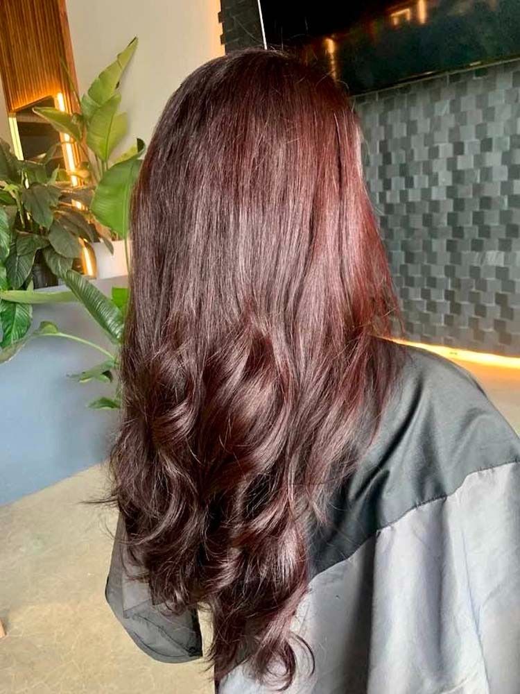 Woman with long, wavy auburn hair. Standing inside, near greenery.